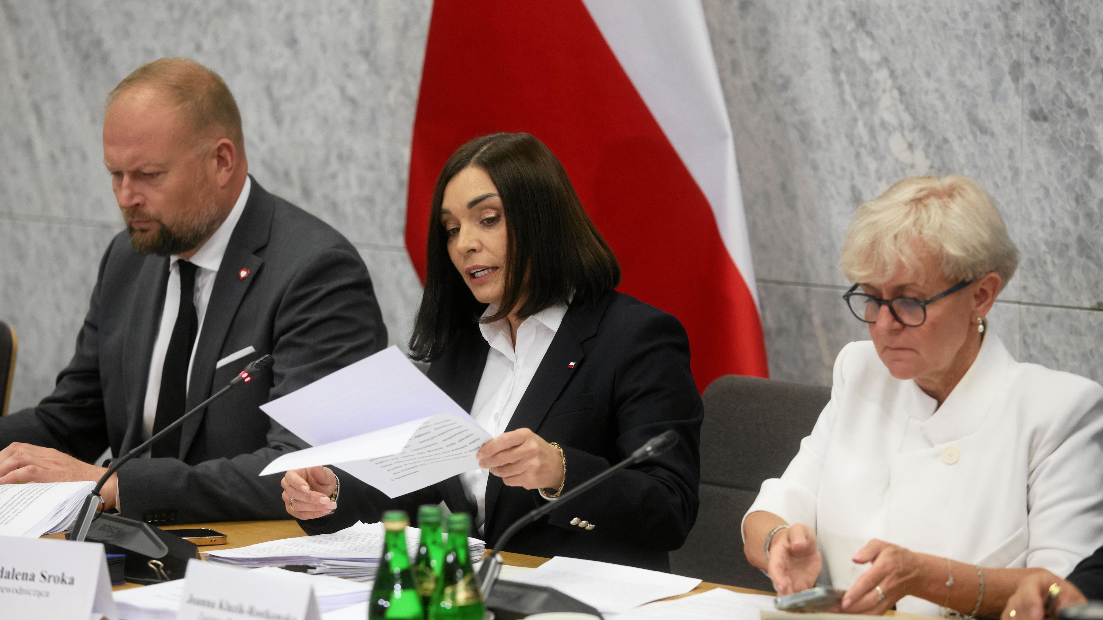 Dwie kobiety i mezczyzna. Kobieta w środku czyta dokument
