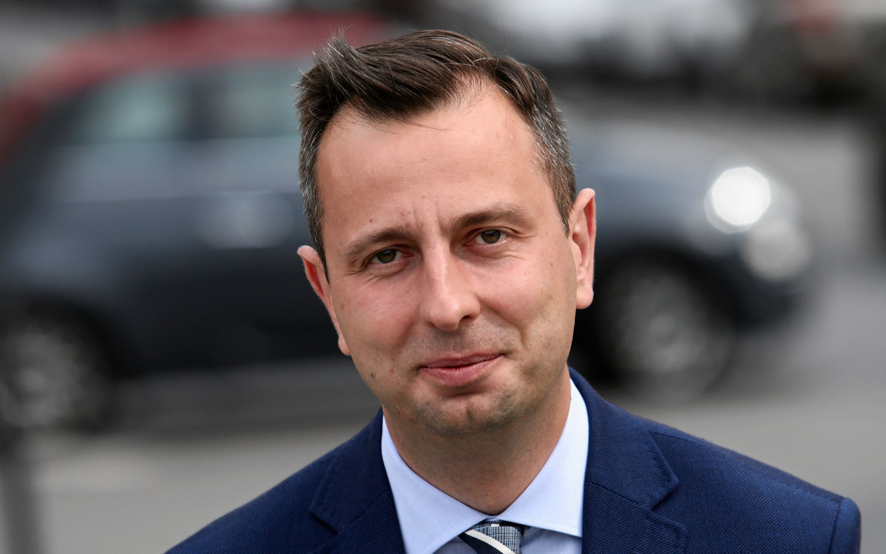 Portret Władysława Kosiniak-Kamysza. stoi na ulicy, w tle rozmazane samochody