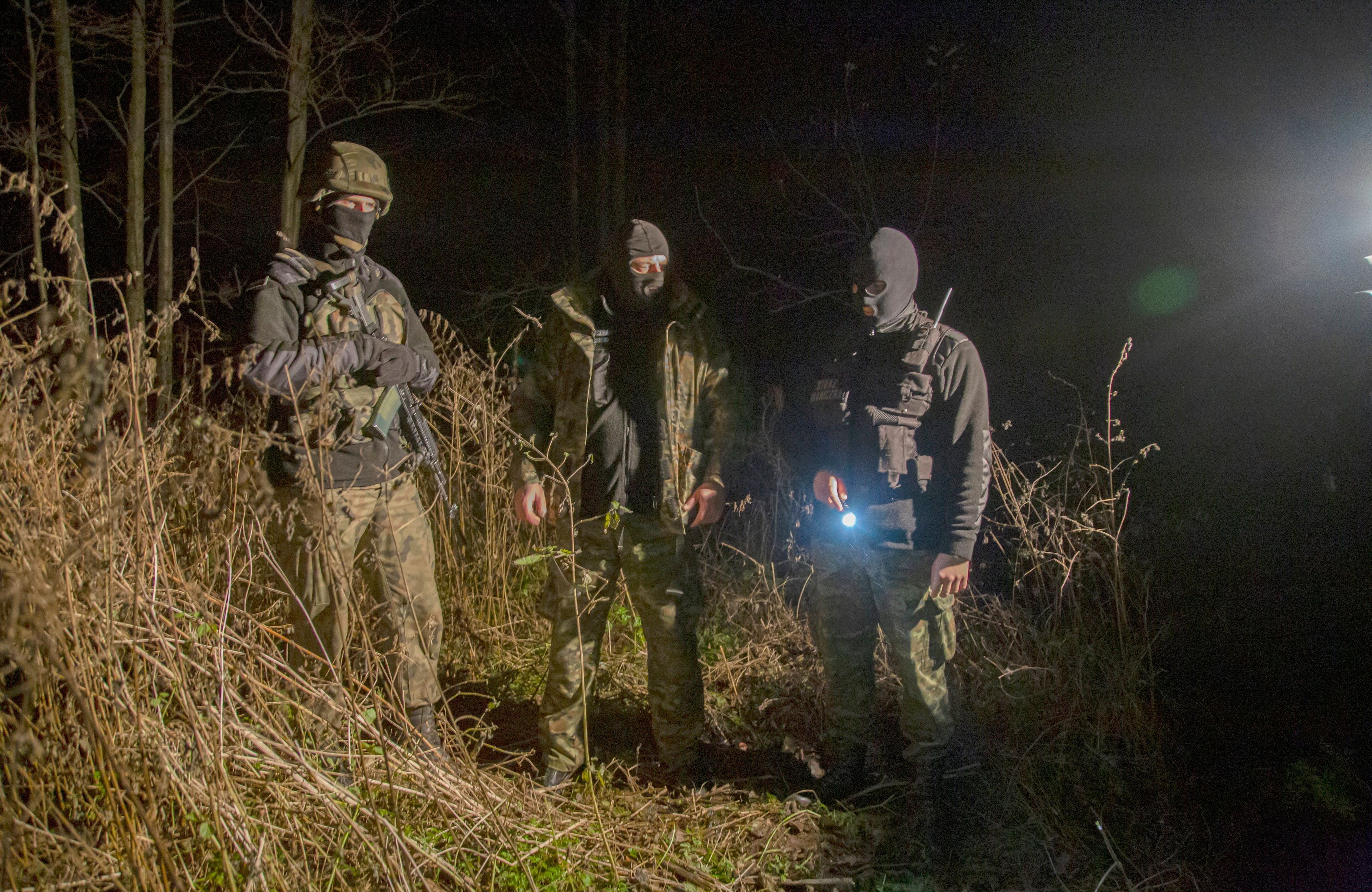 Funkcjonariusze Straży Granicznej świecą latarką w lesie w godzinach nocnych