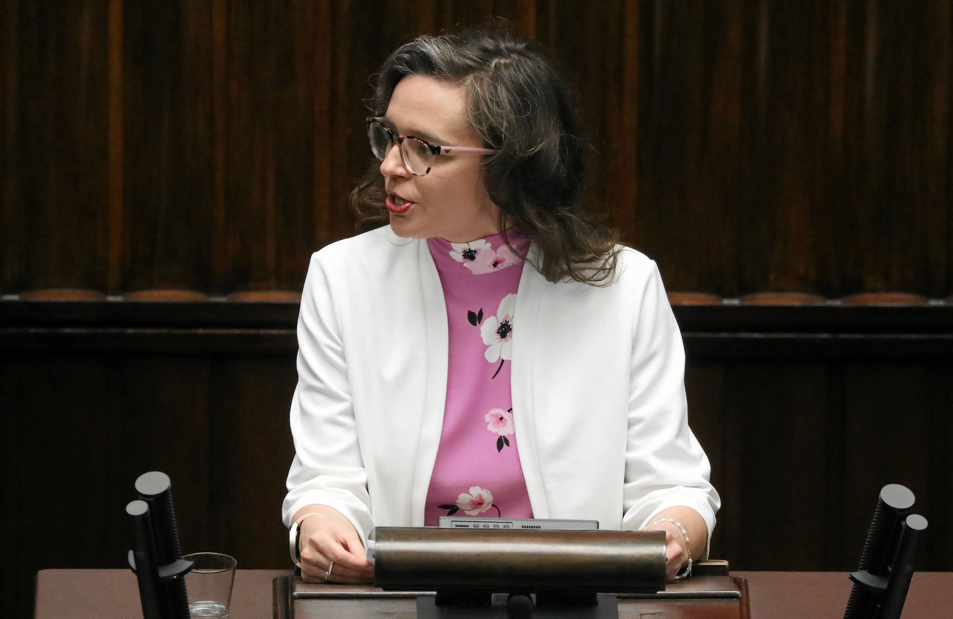 Posłanka Klaudia Jachira w białej marynarce przemawia na mównicy sejmowej