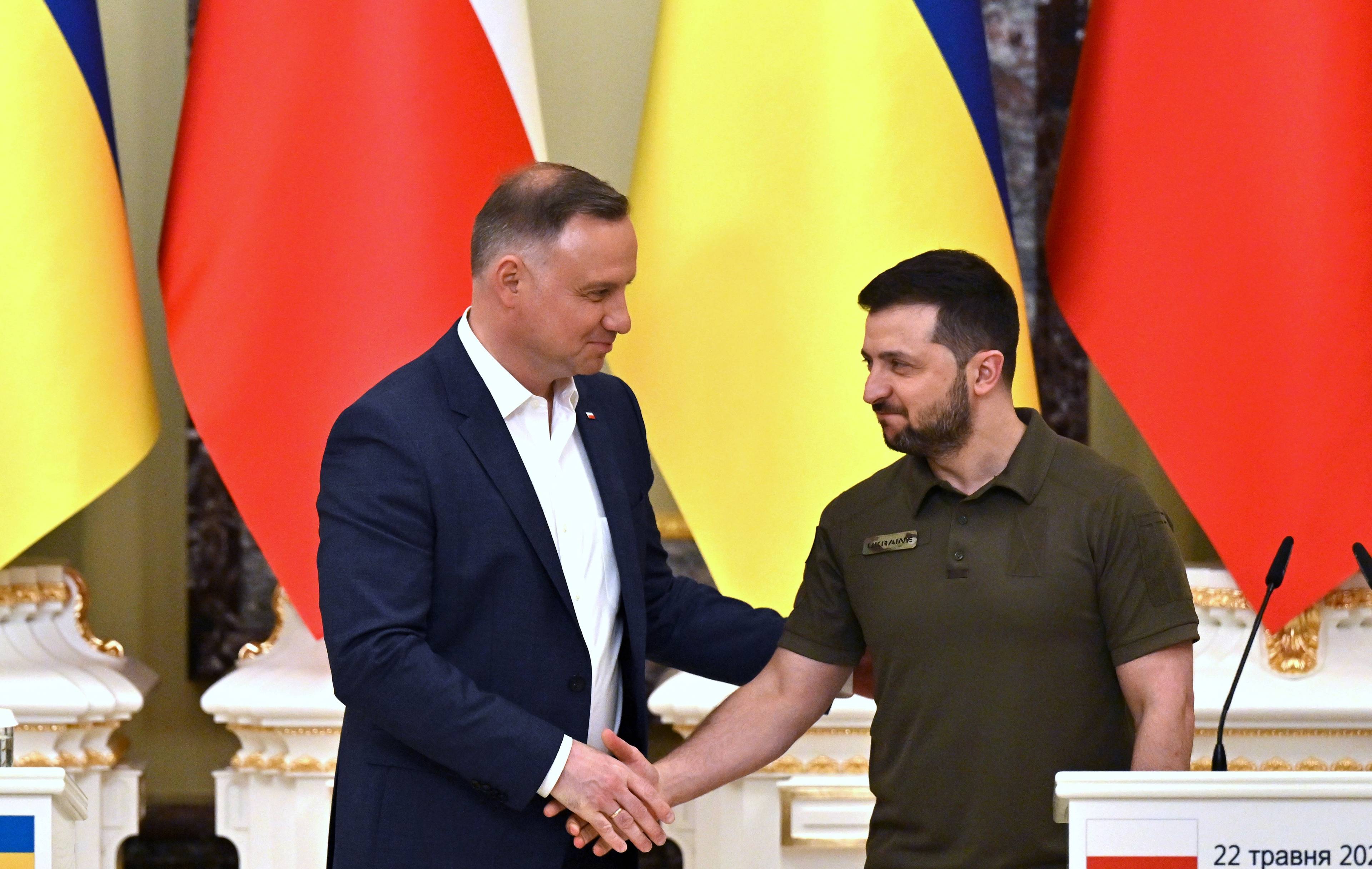Prezydenci Andrzej Duda i Wołodymir Zełenski podają sobie ręce tle flag: ukraińskiej i polskiej