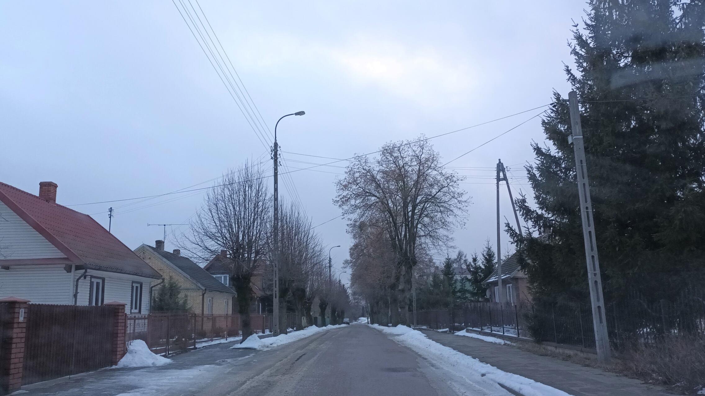 Zdjęcie uliczki w małej miejscowości. Widać niewysokie domy i śnieg