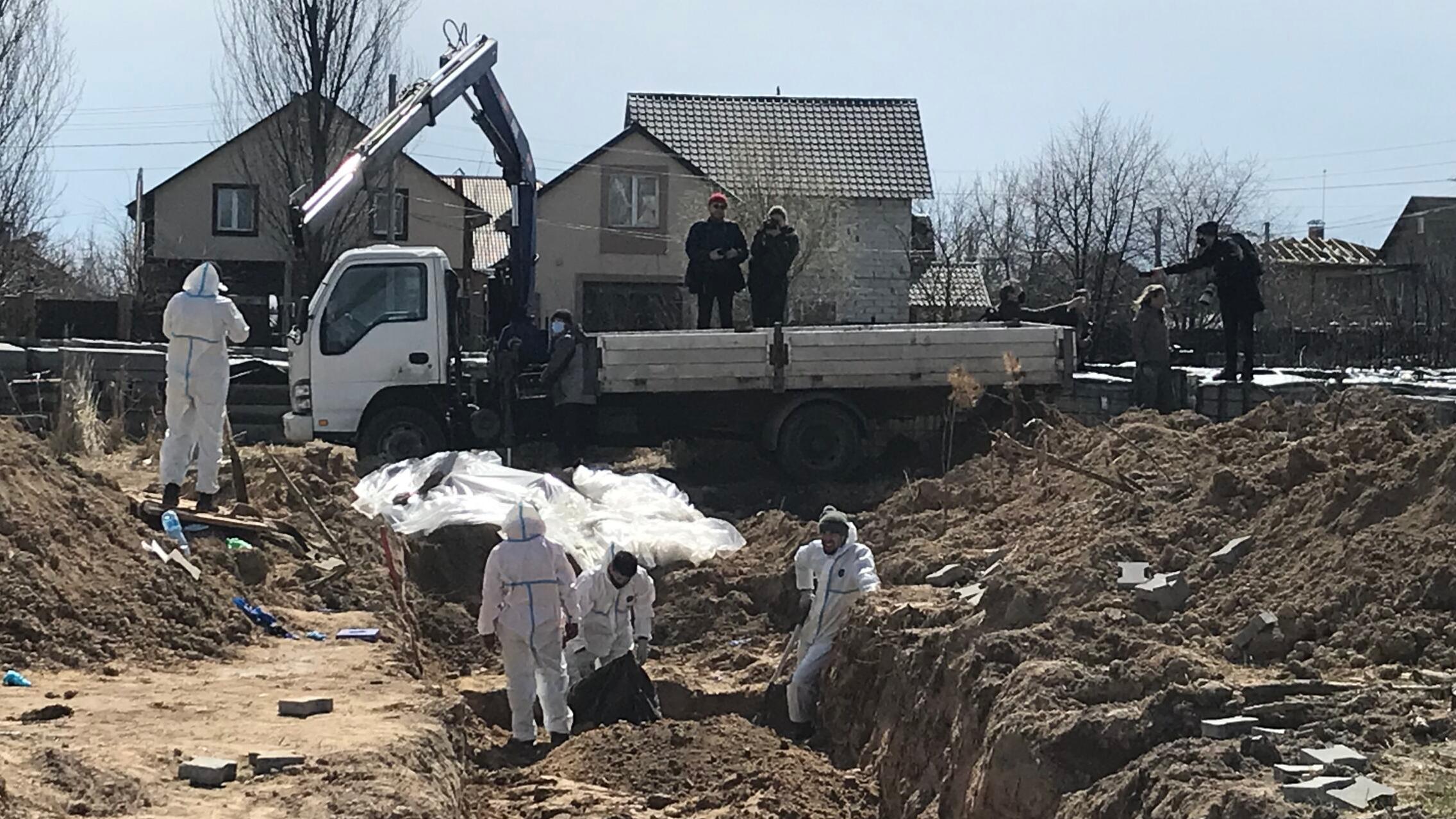 ludzie w białych kombinezonach wydobywają z ziemi ciała ofiar rosyjskiej okupacji Buczy