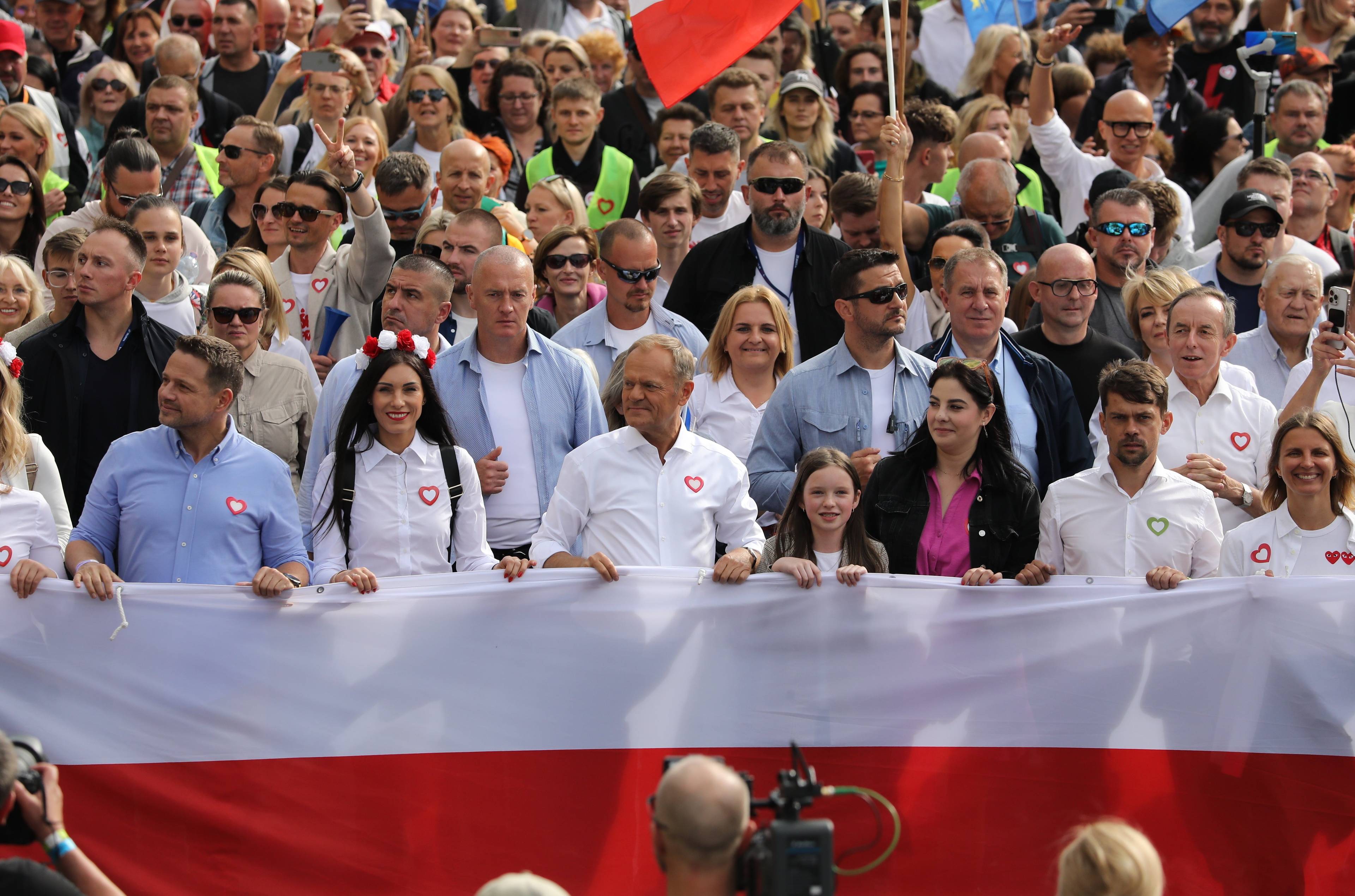 Tłum przechodzący ulicami Warszawy wypełnia zdjęcie, na czele polską flagę trzymają politycy opozycji, wśród nich Donald Tusk