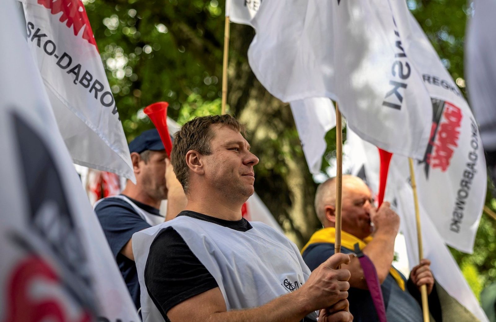 Osoby protestujące przeciwko zwolnieniom w PKP Cargo, w rękach trzymają związkowe flagi