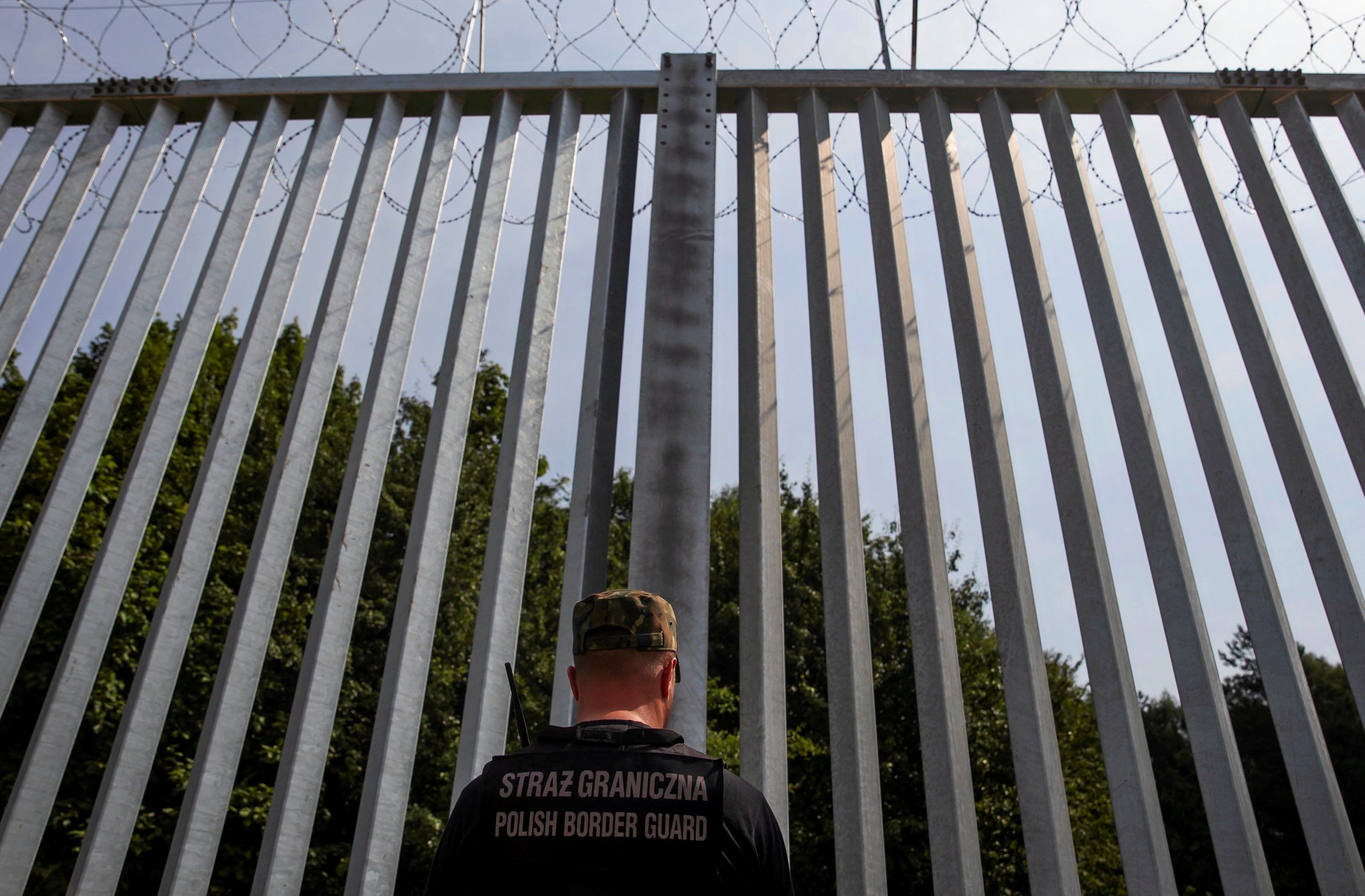 Strażnik graniczny stoi pod wysokim płotem na granicy polsko-białoruskiej. Migranci.