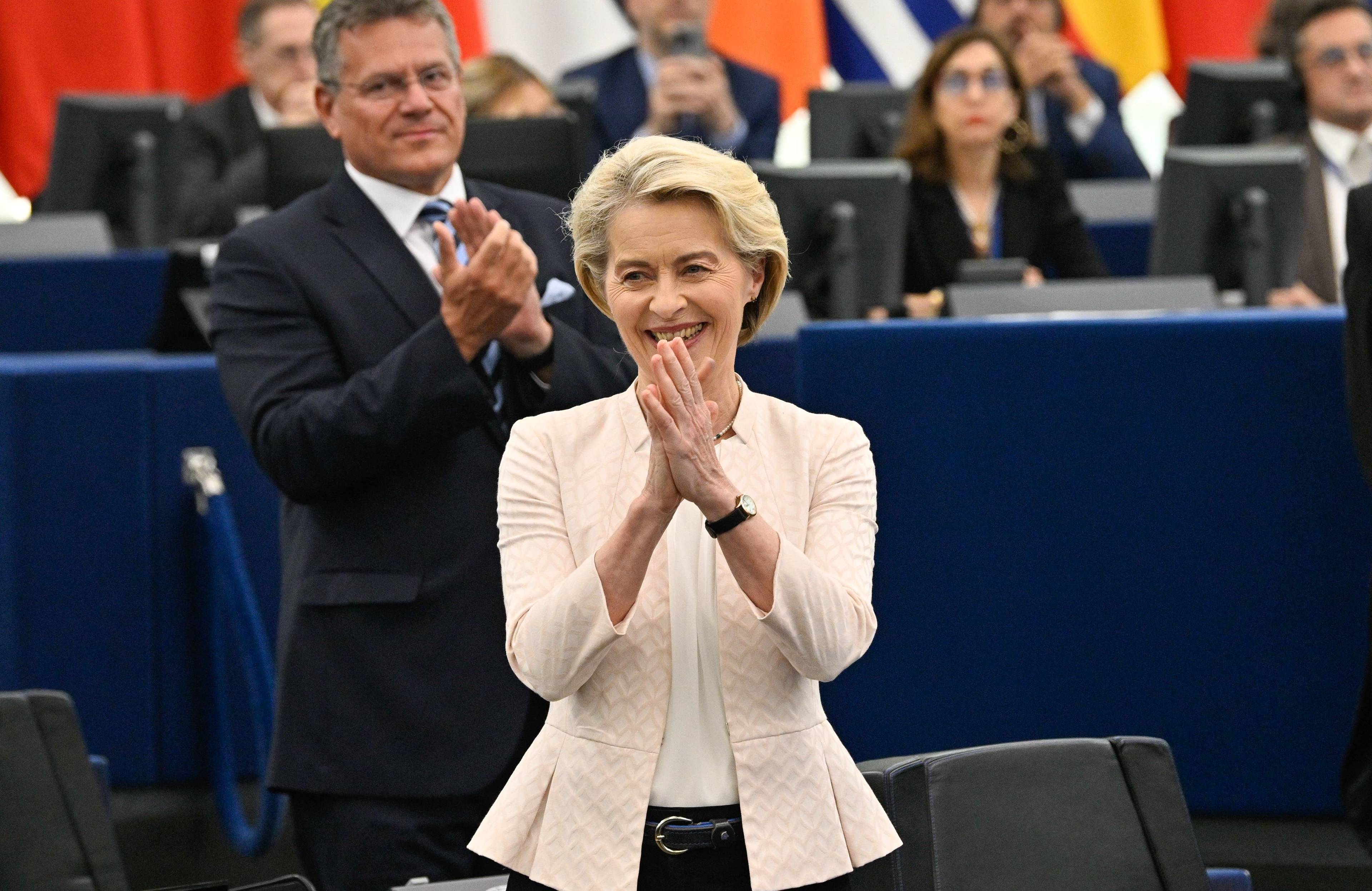 Kobieta z krótkimi blond włosami, jasnej, różowej marynarce, stoi w sali plenarnej PE, uśmiecha się i klaszcze
