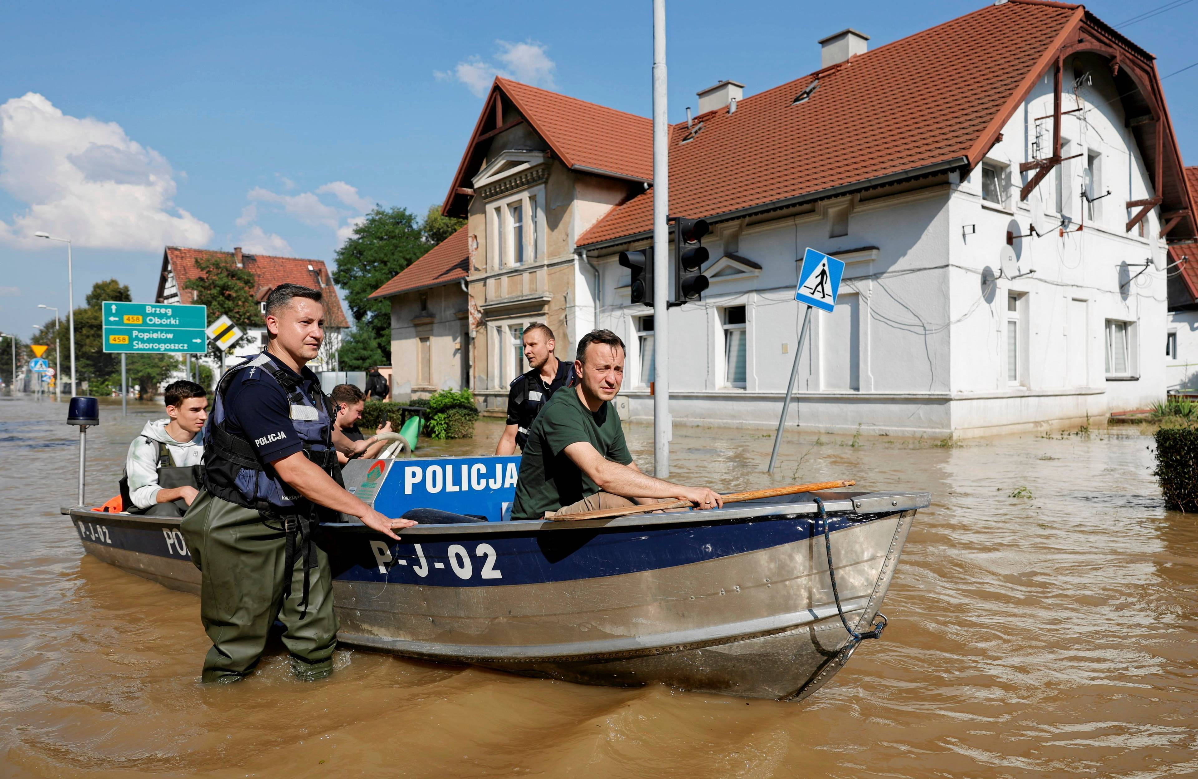 18.09.2024, Lewin Brzeski. Policjanci ubrani w wodery brodzą w wodzie po kolana, prowadząc policyjną łódź.