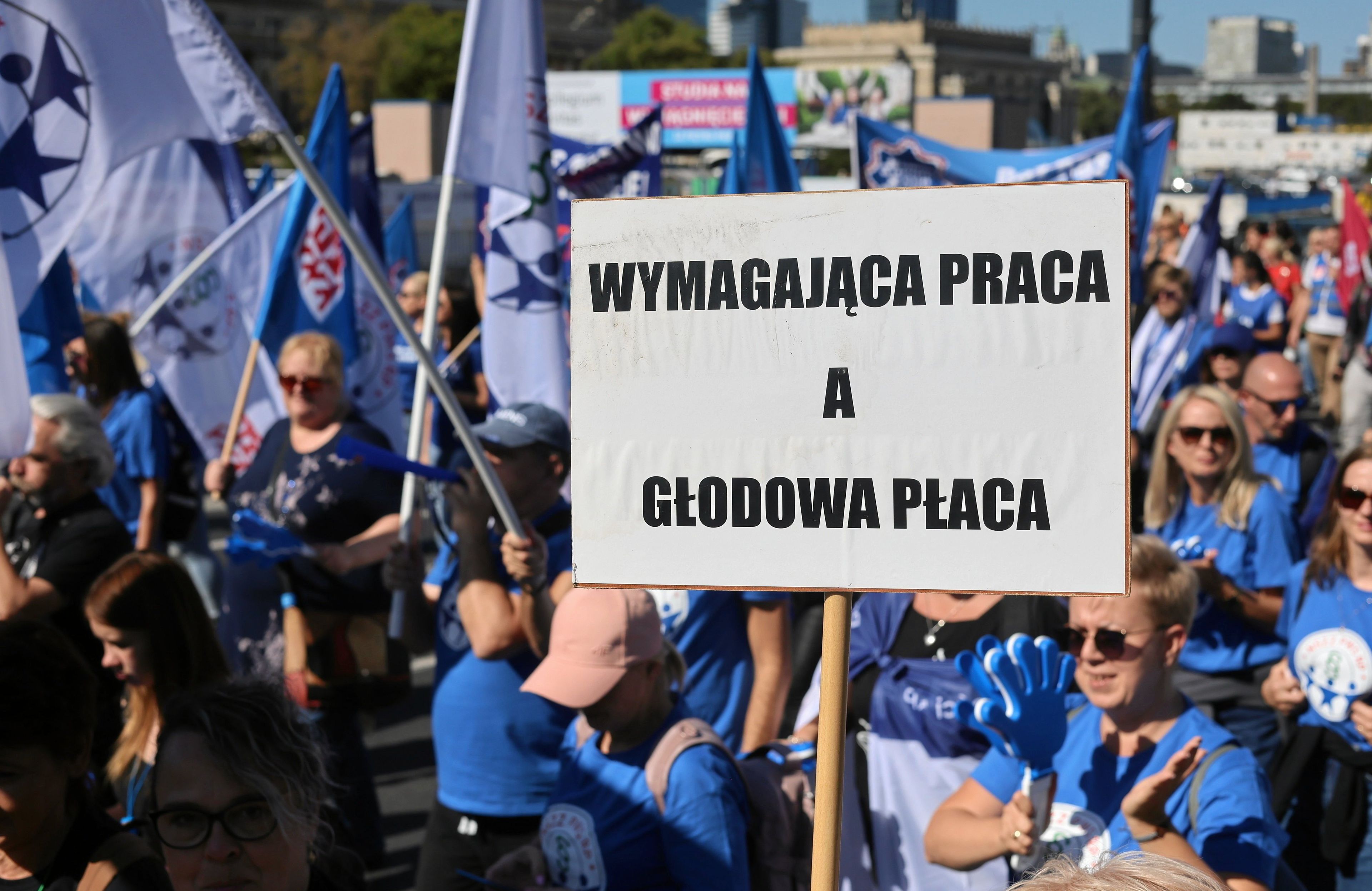 Protest związkowców. Na pierwszym planie transparent "WYmagająca praca a głodowa płaca"