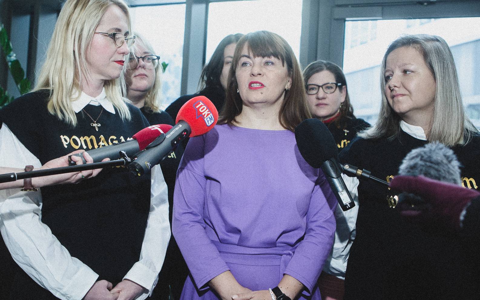 Kobieta w liliowej sukni (Justyna Wydrzyńska) i dwie aktywistki przed mikrofonami dziennikarzy