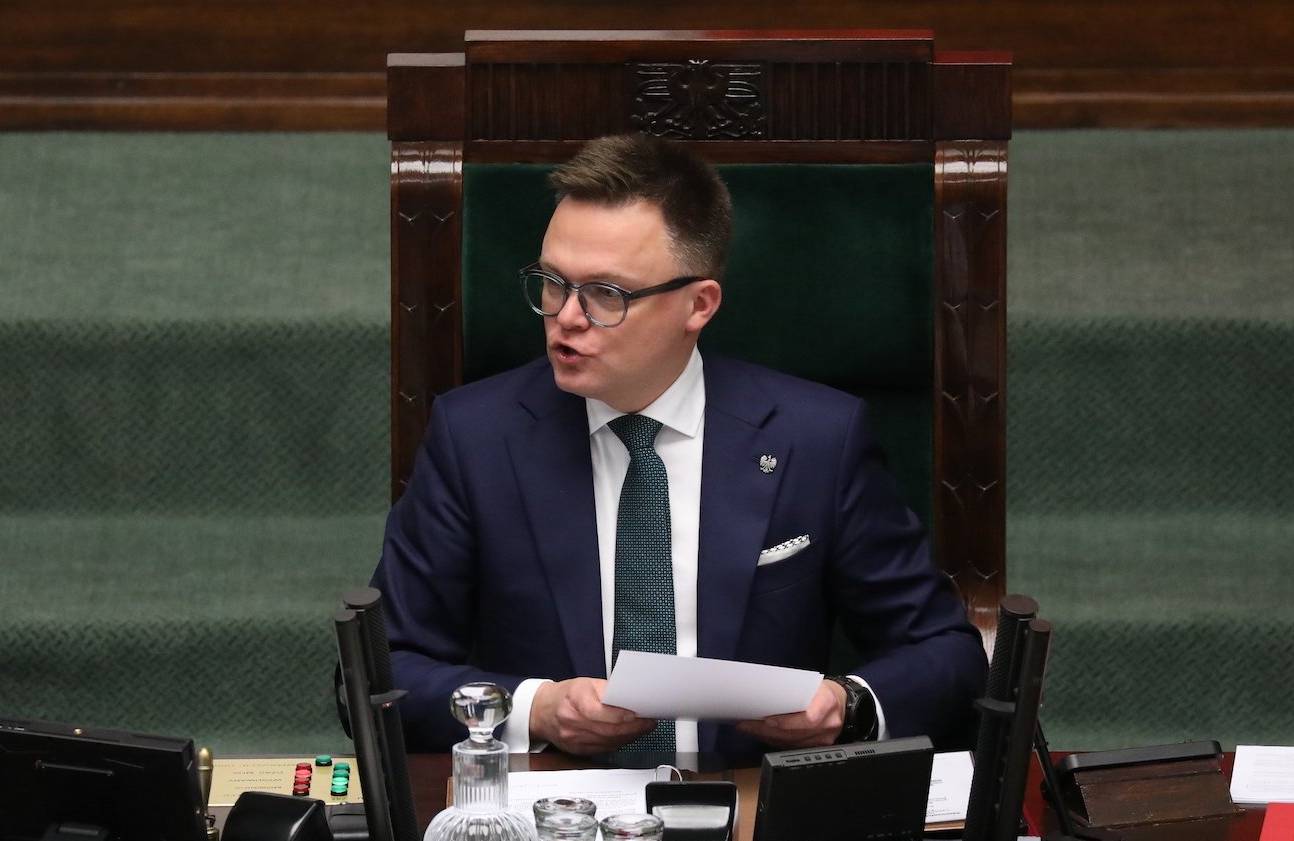 Marszałek Sejmu Szymon Hołownia w fotelu marszałka Sejmu, po lewej laska marszałkowska