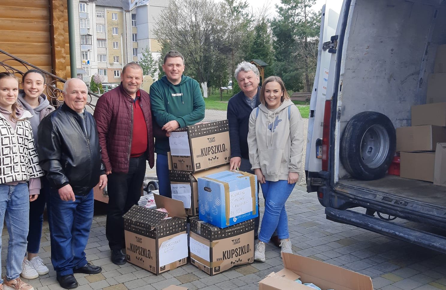Grupa osób z paczkami przy samochodzie. W środku - mężczyzna w zielonej bluzie (Marek Klara, były burmistrz gminy Miejsce Piastowe)