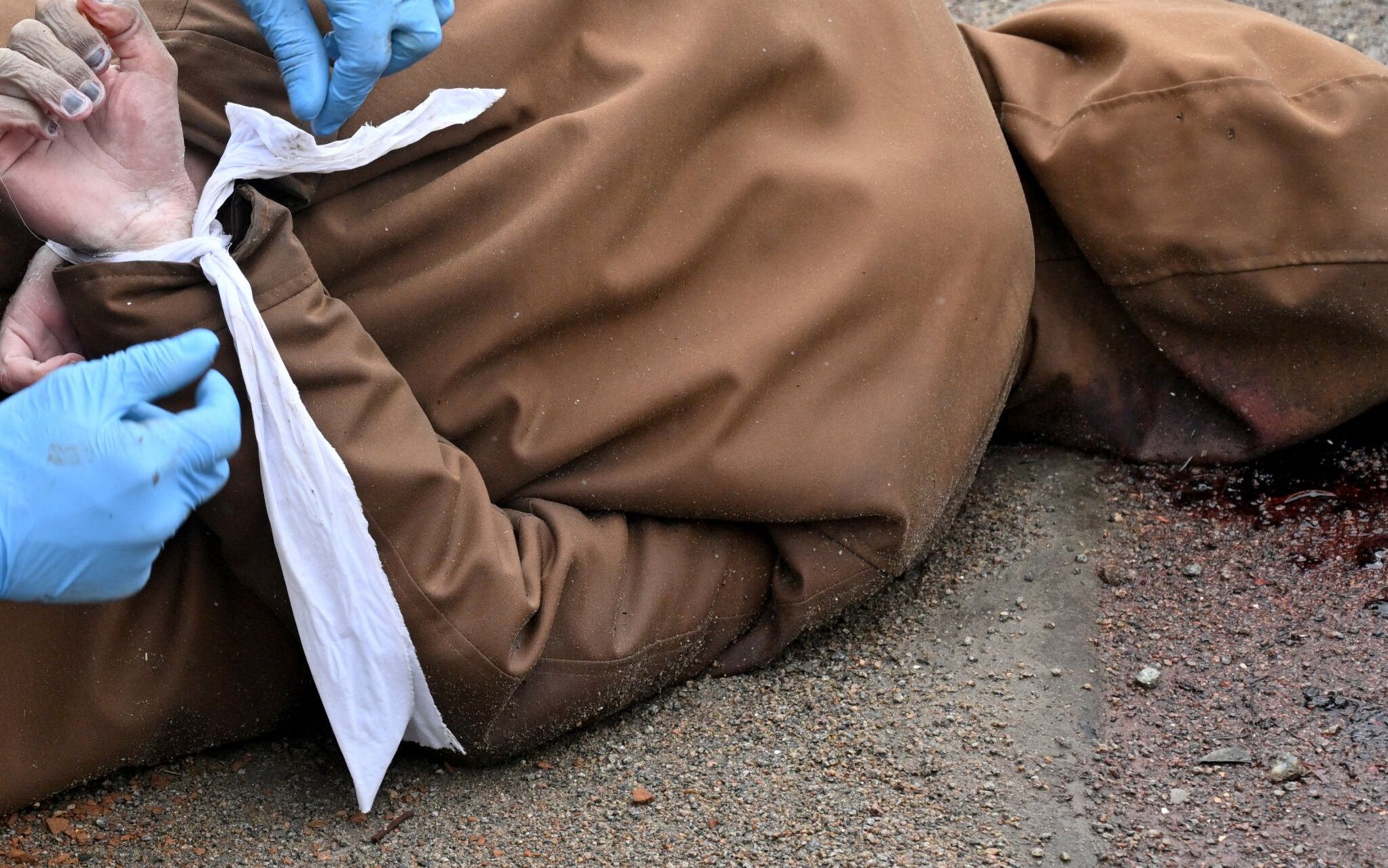 EDITORS NOTE: Graphic content / A communal worker releases the wrists of a dead man, with his hands tied behind his back, in the town of Bucha, not far from the Ukrainian capital Kyiv on April 3, 2022. - President Volodymyr Zelensky accused Russia of committing genocide and attempting to eliminate the "whole nation" of Ukraine, a day after the discovery of mass graves and apparently executed civilians near Kyiv. Ukraine has recovered 410 civilian bodies from areas it recently retook from the Russian army in the wider Kyiv region, its prosecutor general Iryna Venediktova said Sunday. (Photo by Sergei SUPINSKY / AFP)