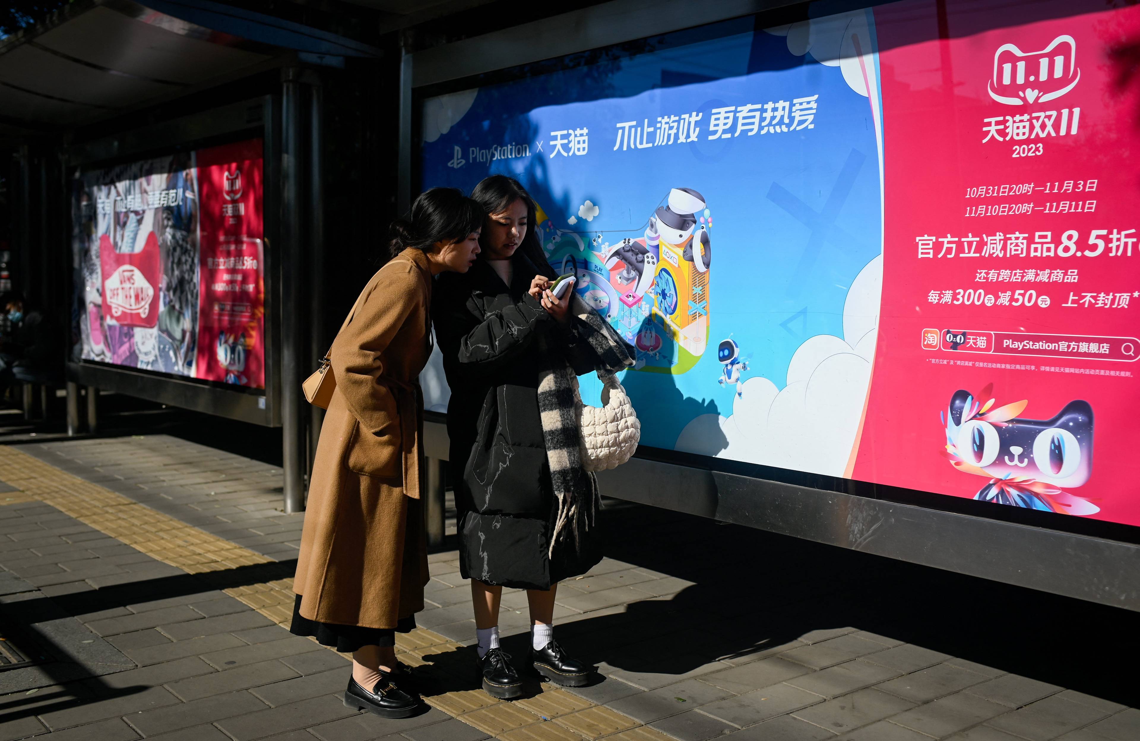 dwie Azjatki sprawdzające coś w komórce, w tle plakat po chińsku