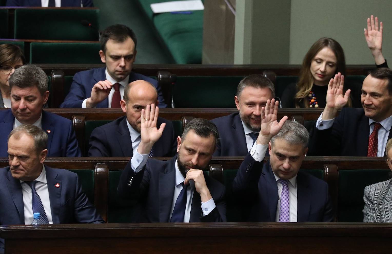 Członkowie rządu KO, Lewicy i Trzeciej Drogi podczas głosowania w Sejmie, unoszą ręce. Na pierwszym planie m.in. Donald Tusk.