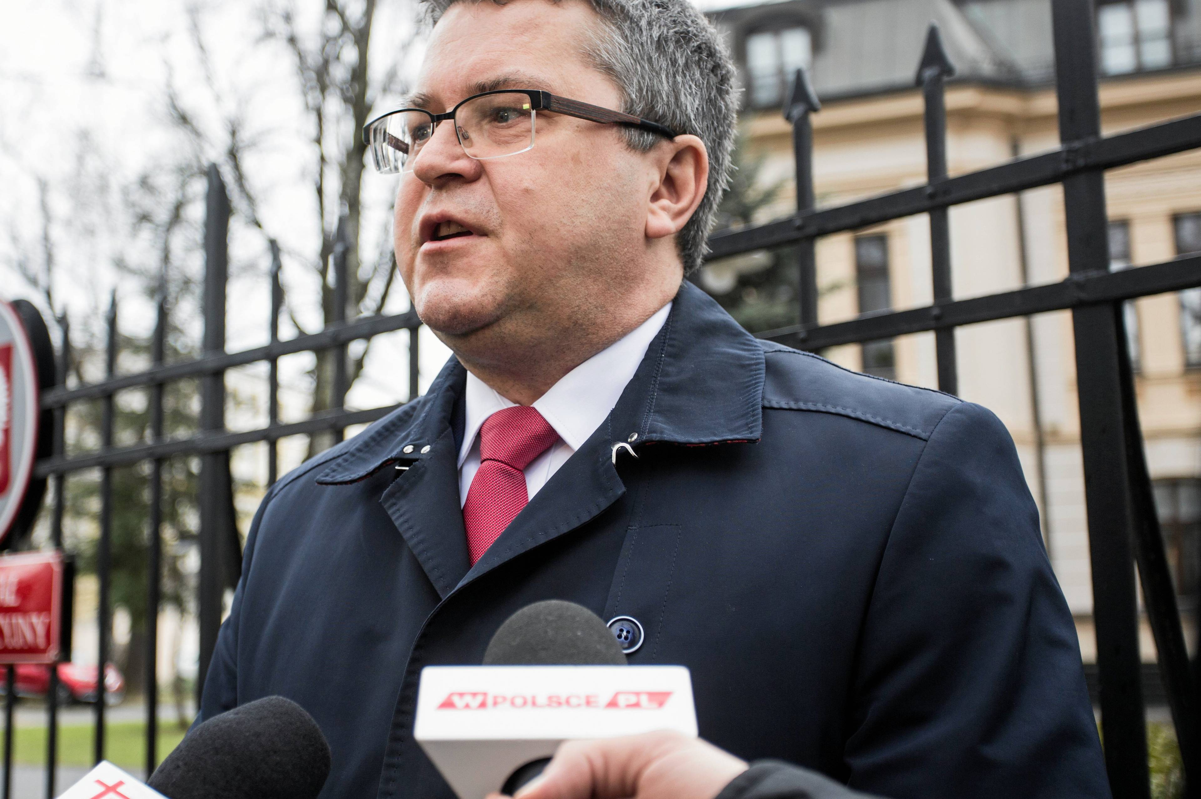 Mężczyzna w okularach stoi na tle metalowego płotu Trybunału Konstytucyjnego. Jarosław Dudzicz