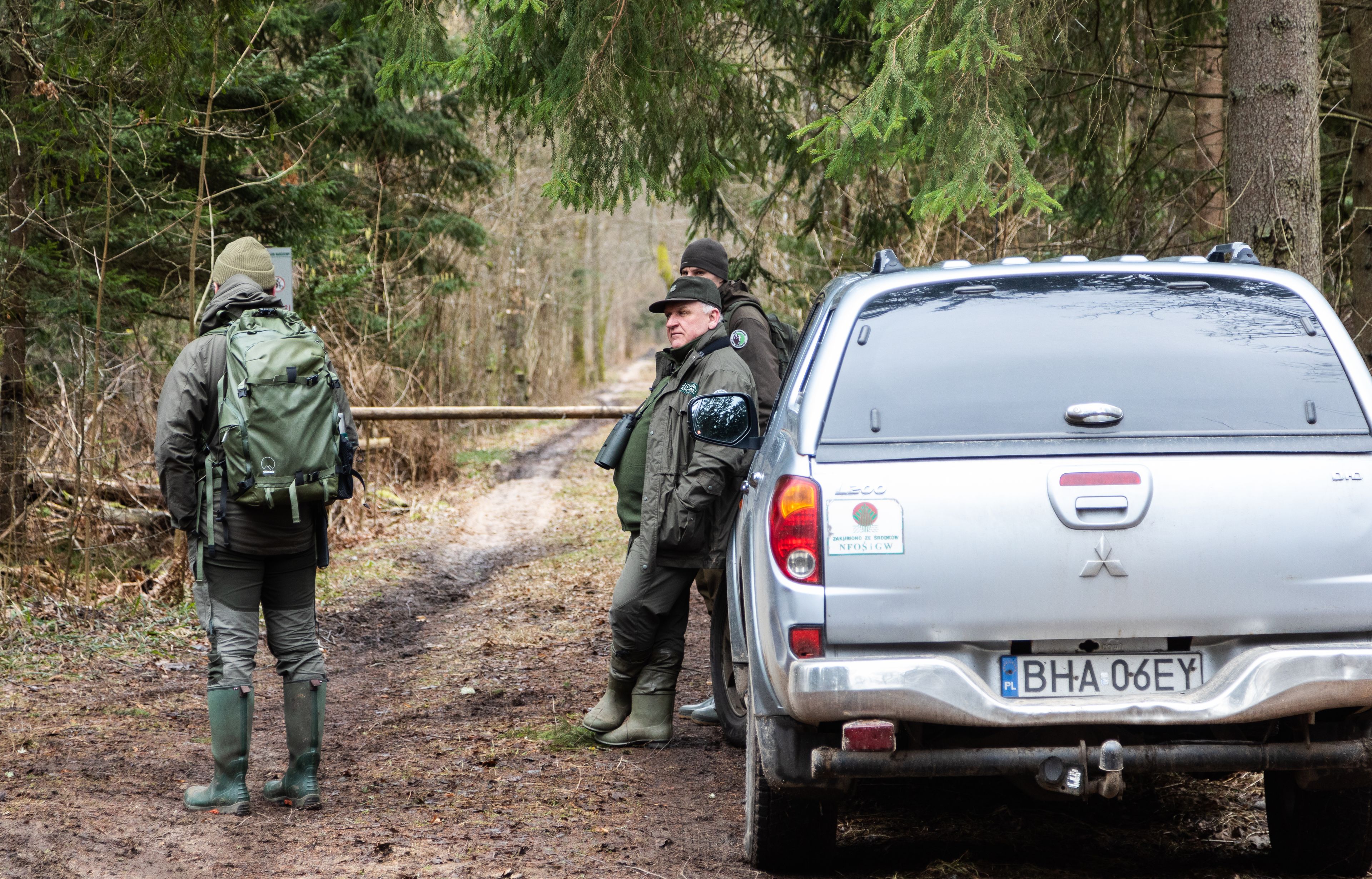 Leśna droga, szlaban, strażnicy blokują - stja oparci o samochód terenowy.