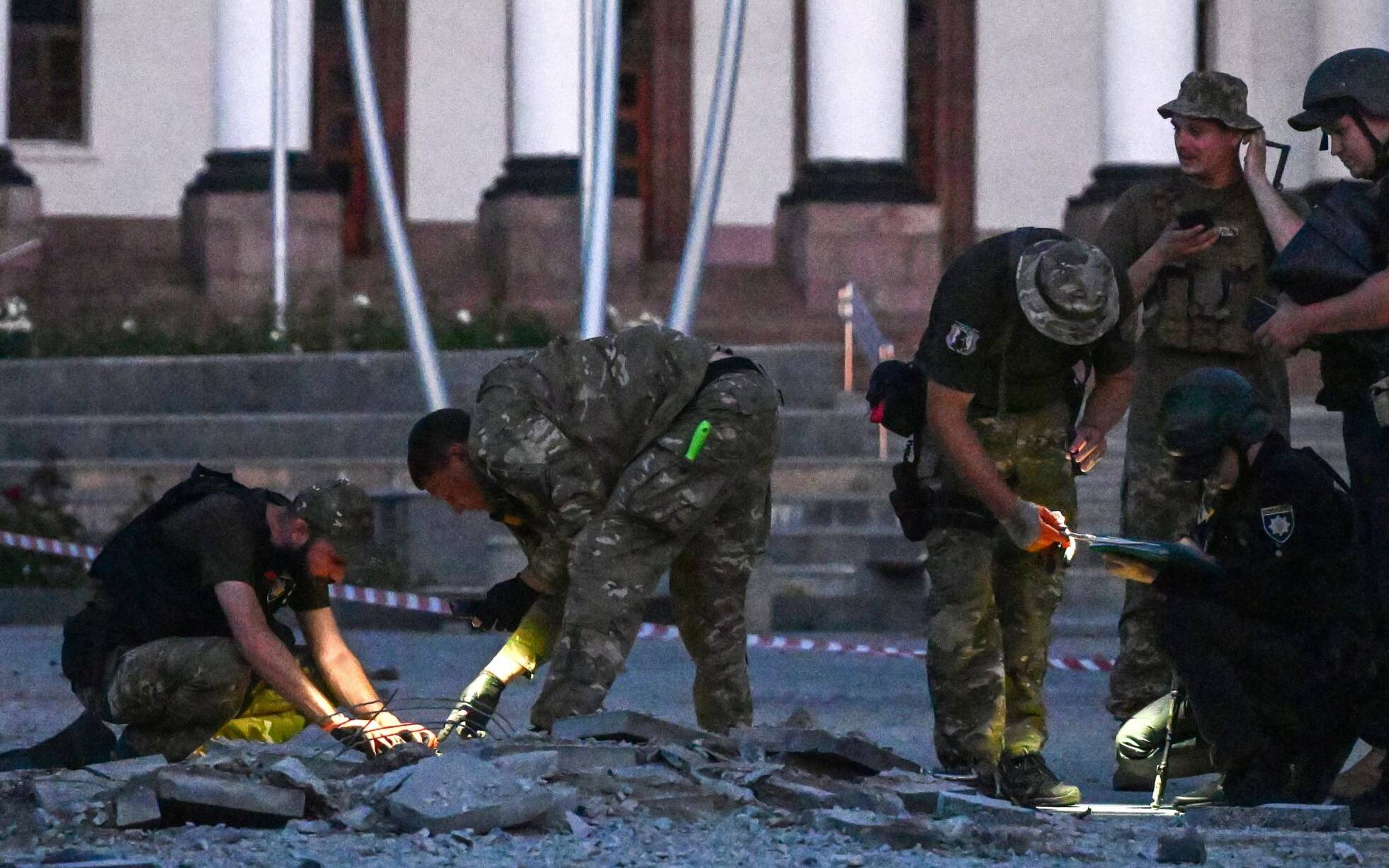 Ukrainian servicemen inspect the damaged ground of a street after an air strike hit the Myru (Peace) square in front of the Palace of Culture and Technology and the City Hall in the center of Kramatorsk on July 15, 2022, amid the Russian invasion of Ukraine. (Photo by MIGUEL MEDINA / AFP)