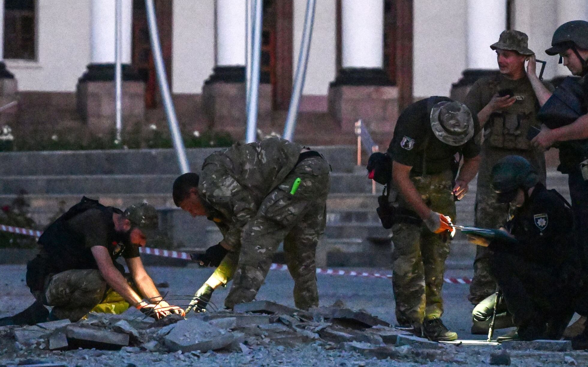 Ukrainian servicemen inspect the damaged ground of a street after an air strike hit the Myru (Peace) square in front of the Palace of Culture and Technology and the City Hall in the center of Kramatorsk on July 15, 2022, amid the Russian invasion of Ukraine. (Photo by MIGUEL MEDINA / AFP)