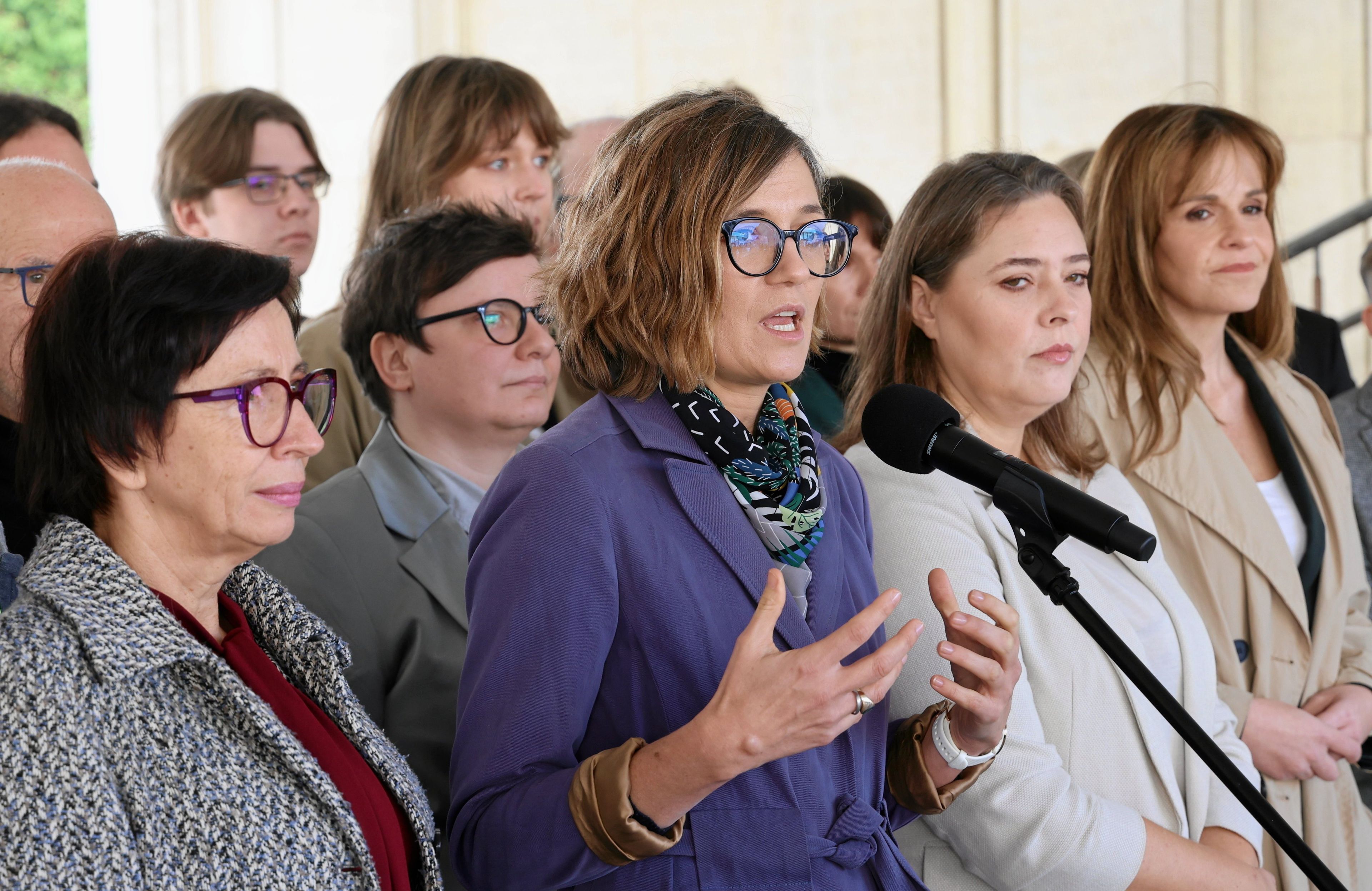 Magdalena Biejat w fioletowym płaszczu przemawia przez mikrofon przed budynkiem Senatu. Obok niej stoi senatorka Anna Górska. Na zdjęciu widzimy też posłanki - Dorota Olko, Joanna Wicha. Na drugim planie działacze i działaczki Lewicy Razem