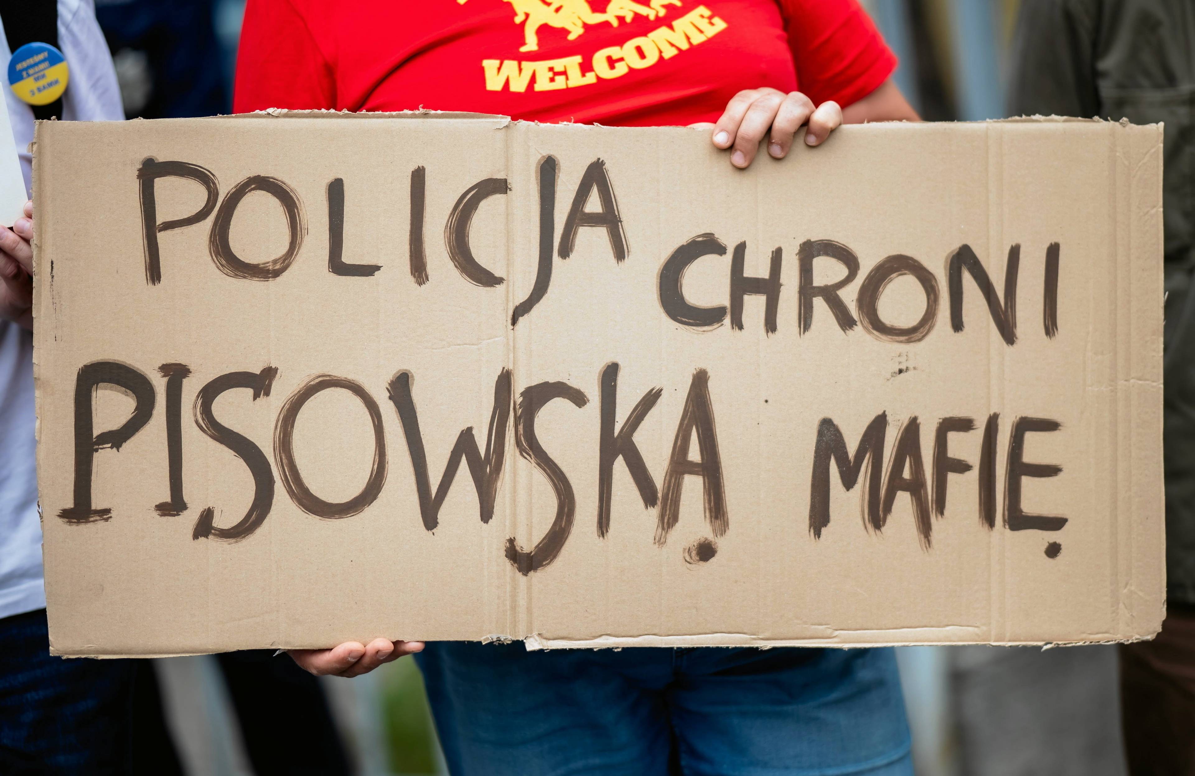 Niewidoczna na zdjęciu osoba trzyma plakat „Policja chroni pisowską mafię"