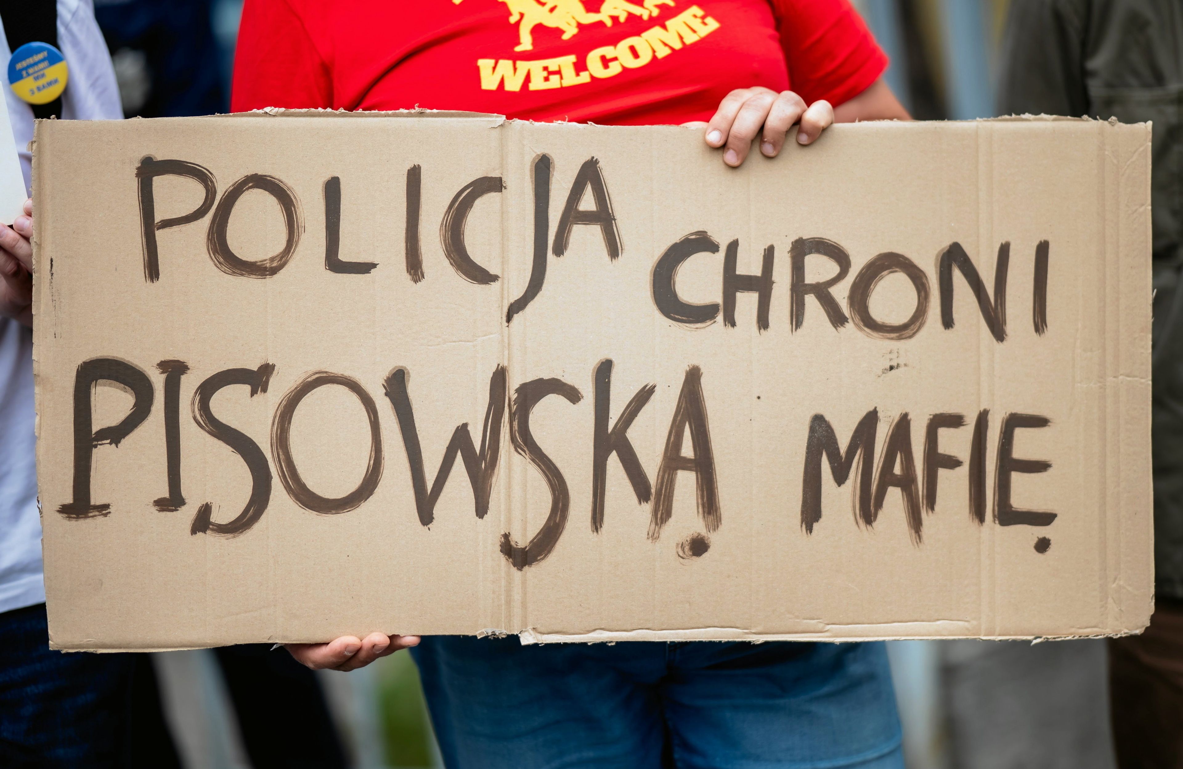 Niewidoczna na zdjęciu osoba trzyma plakat „Policja chroni pisowską mafię"