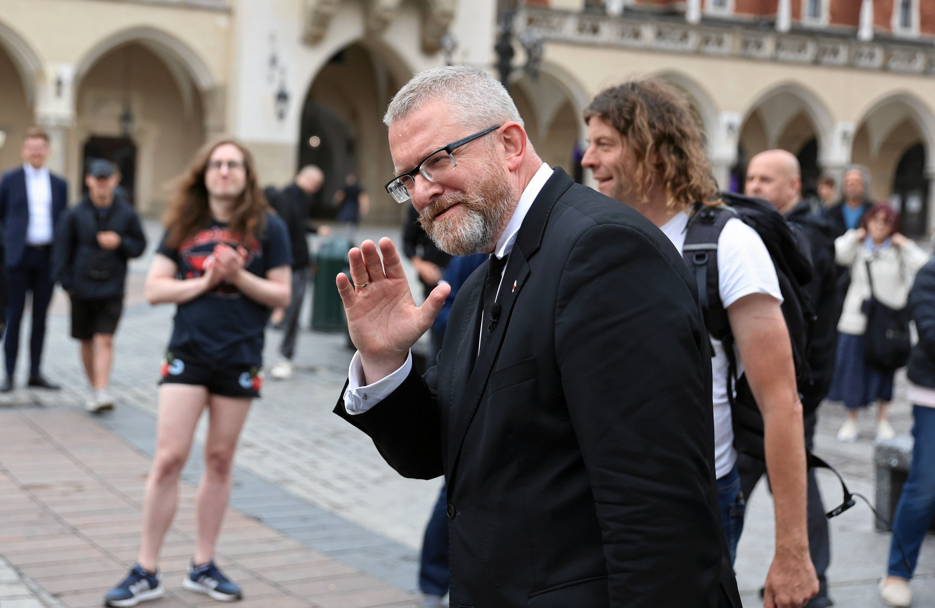 Siwy mężczyzna w okularach, w średnim wieku, na środku rynku w Krakowie.