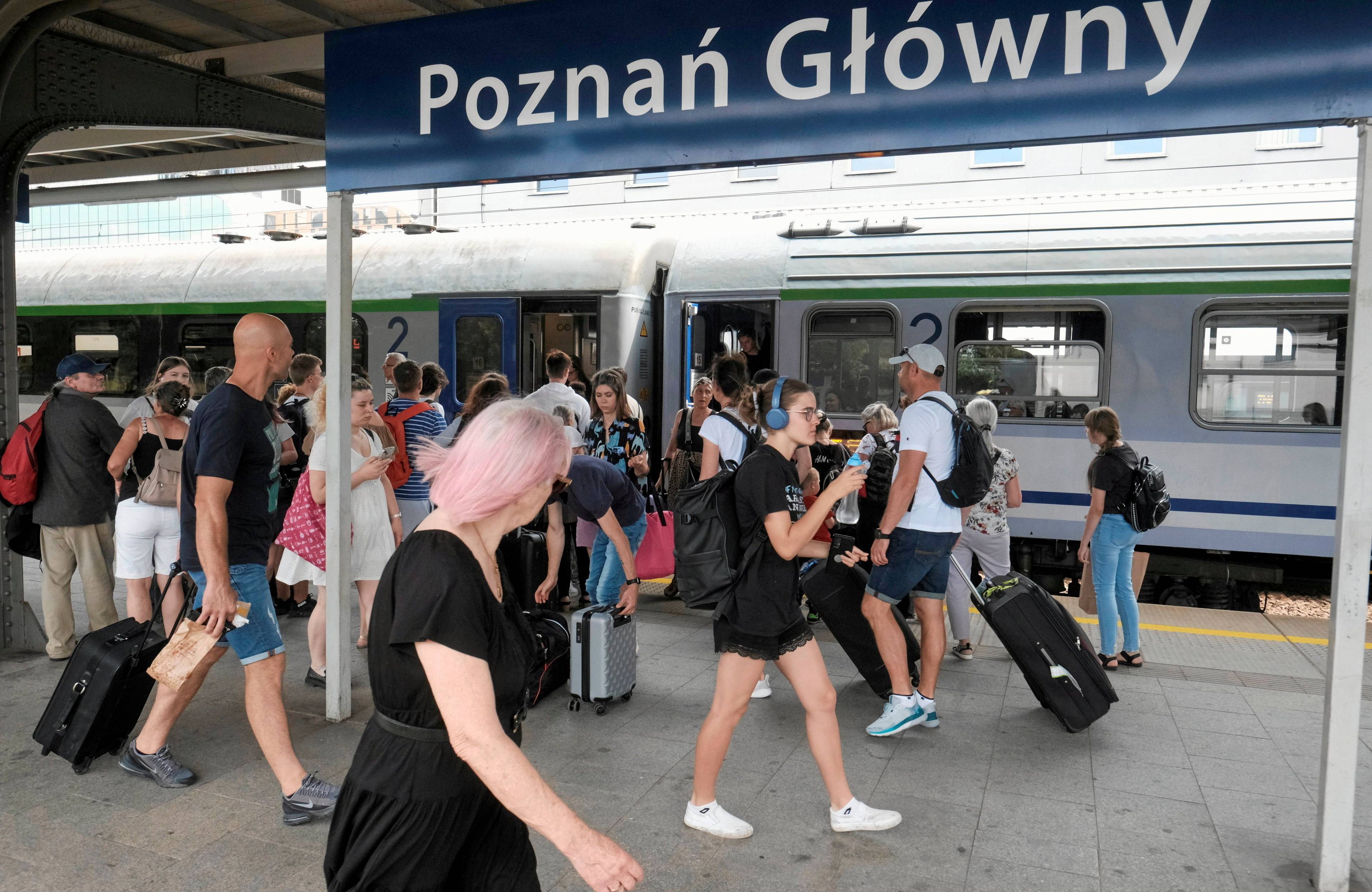 peron na stacji Poznań Główny, idący przez niego podróżni i napis "poznań główny"