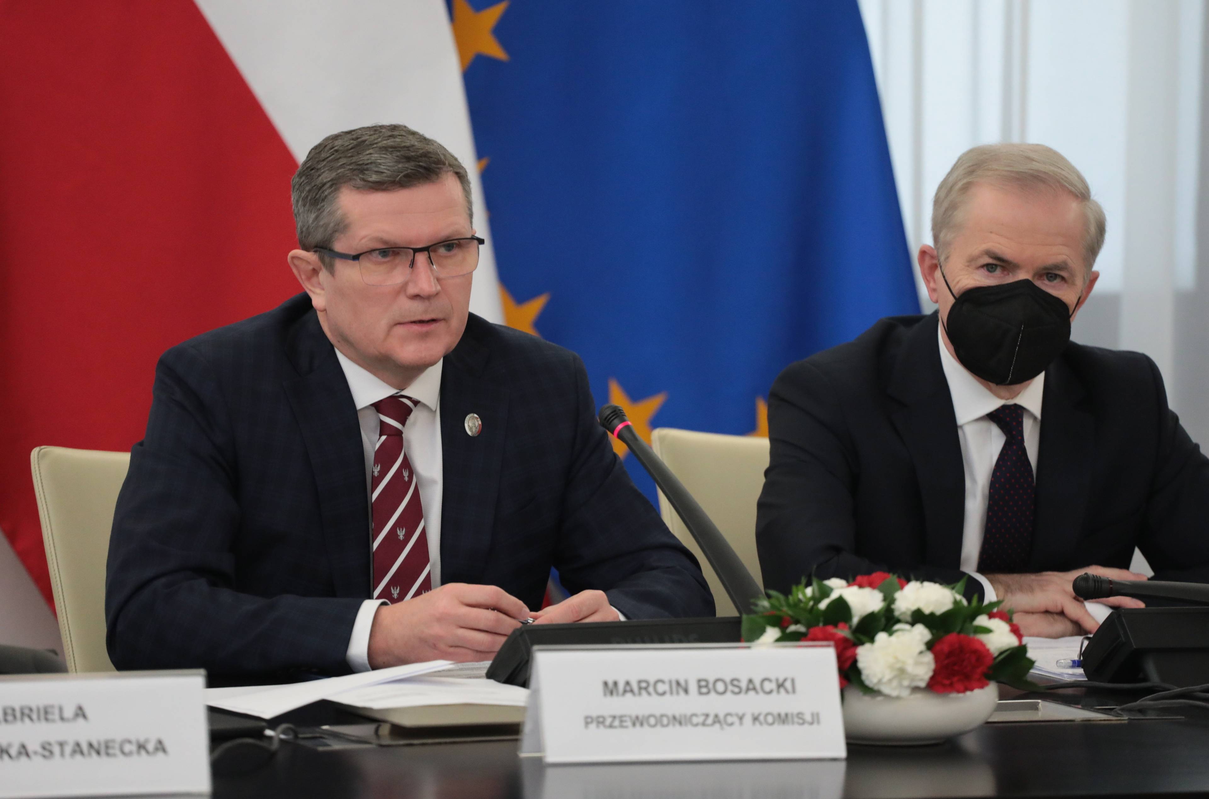 Mężczyzna siedzi, na stole przed nim tabliczka "Marcin Bosacki, przewodniczący komisji"