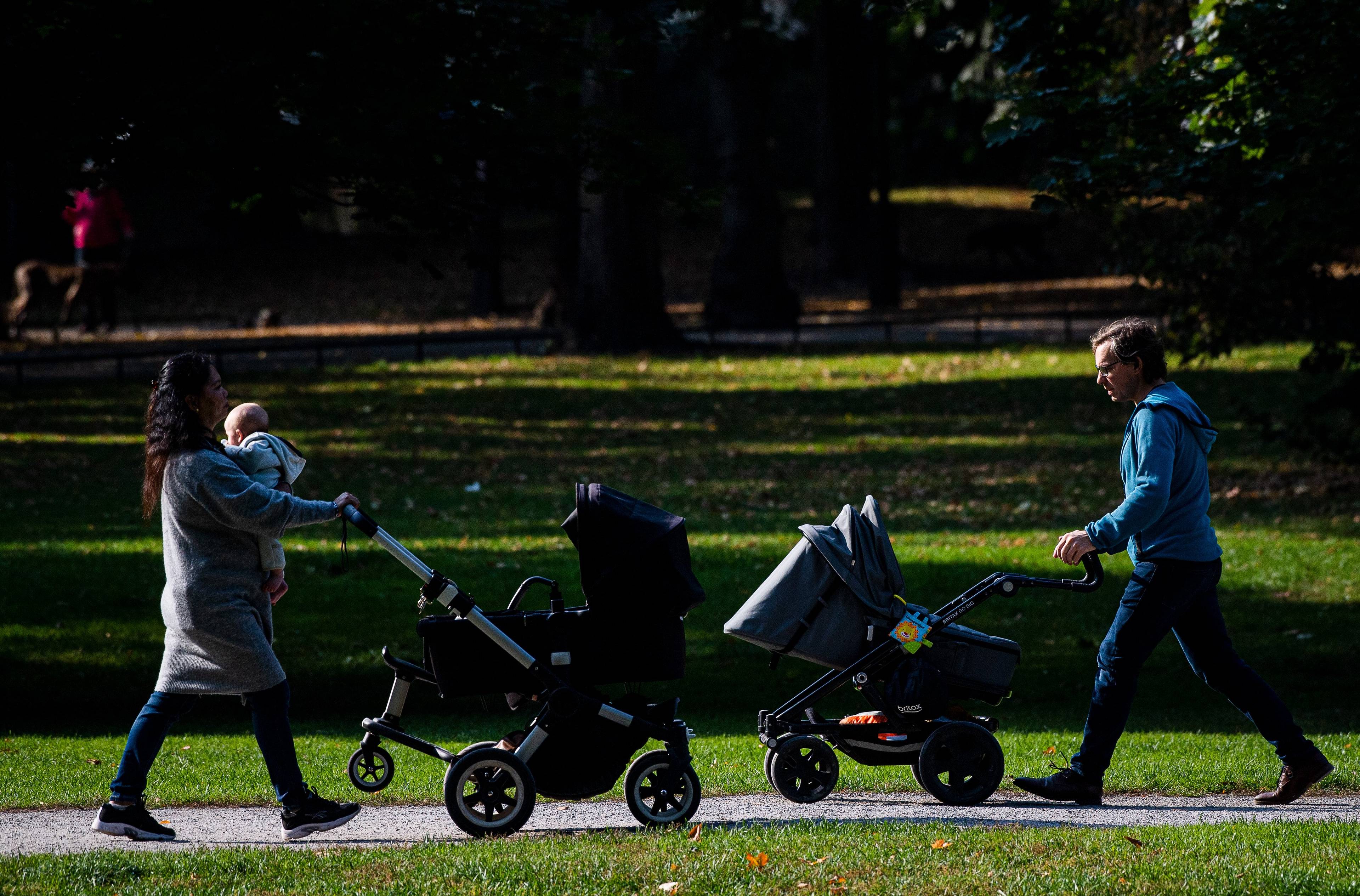 Kobieta i mężczyzna w parku w Sztokholmie, mijają się z naprzeciwka, prowadząc dziecięce wózki