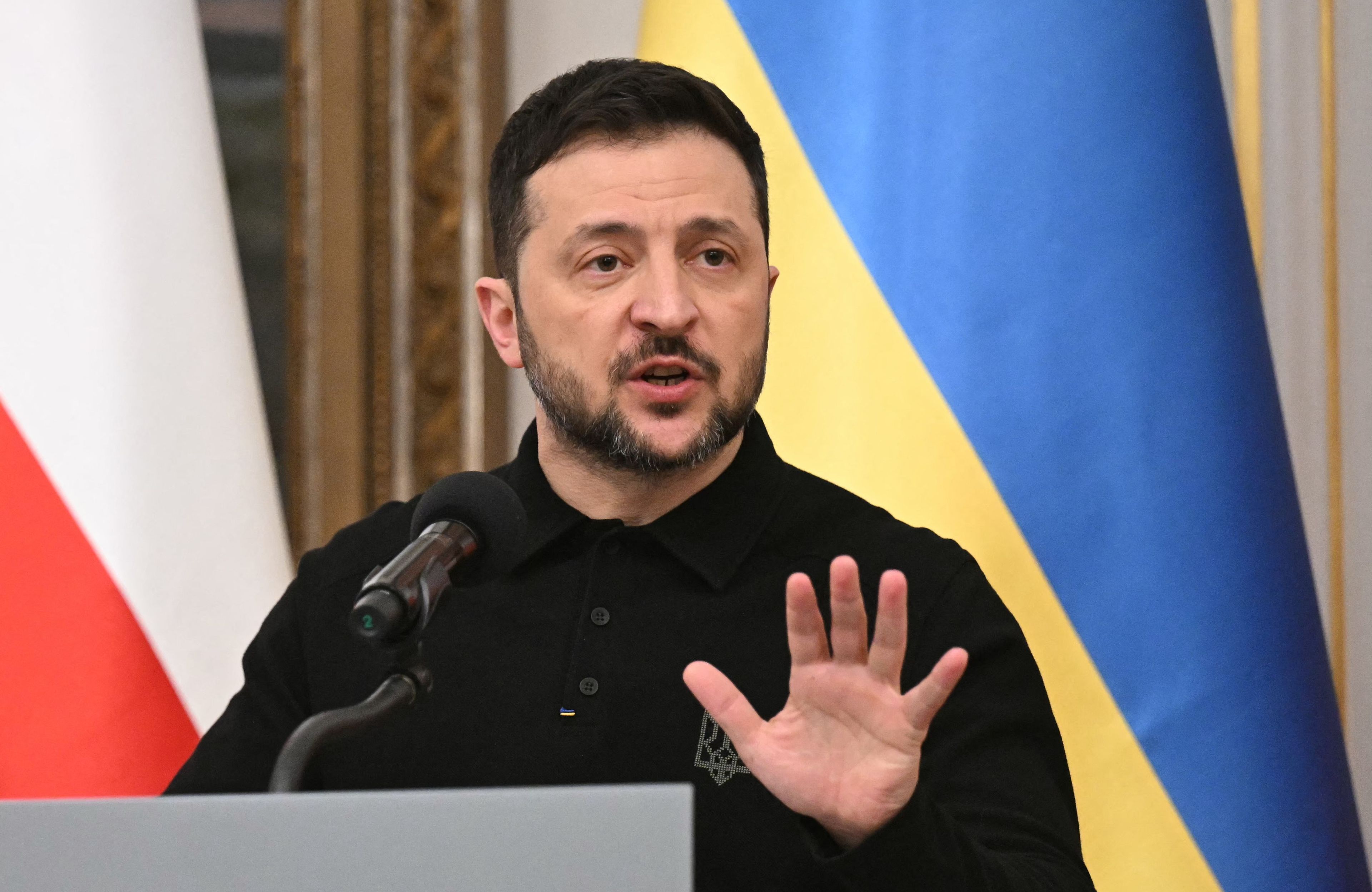 Prezydent Ukrainy Wołodymyr Zełenski podczas przemówienia, na tle ukraińskiej flagi