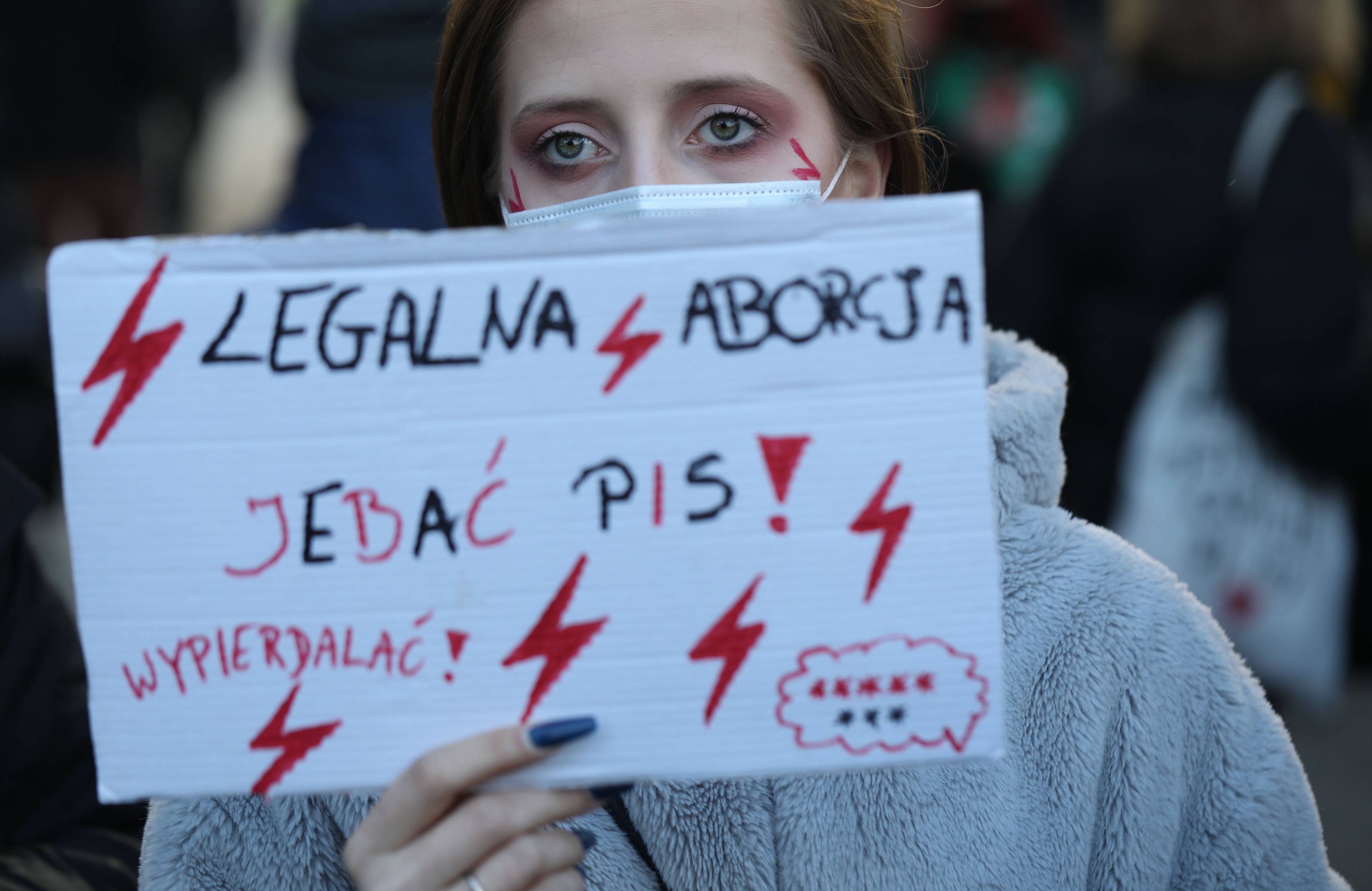 Uczestniczka protestu trzyma na wysokości twarzy kartkę z napisami Legalna aborcja, jebać PiS,wypierdalać i ośmioma gwiazdkami. Gniew kobiet
