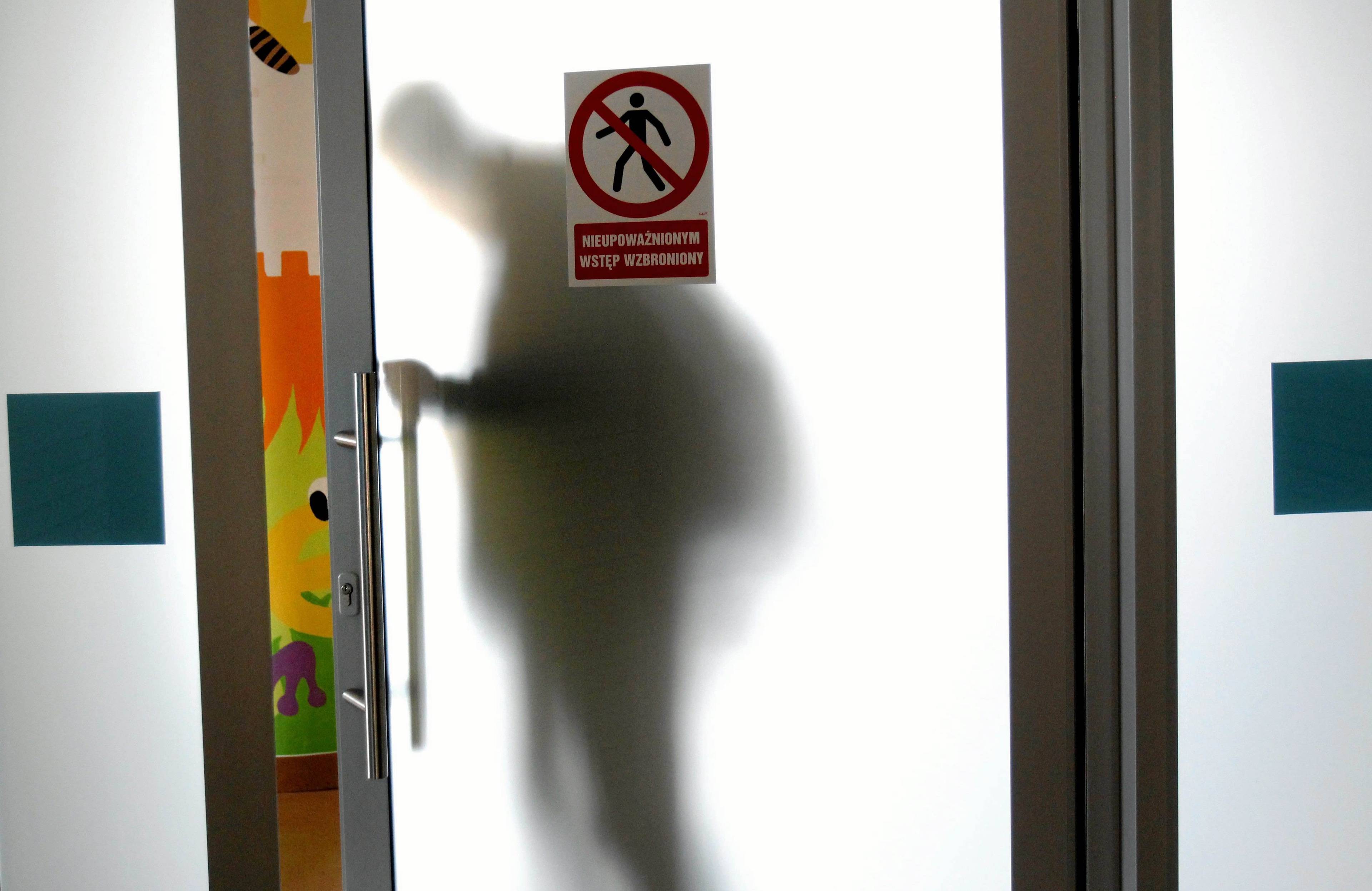 Drzwi z mlecznego szkła w placówce szpitalnej, za drzwiami widać cień człowieka, na d drzwiami napis „Nieupoważnionym wstęp wzbroniony” . Choroba genetyczna