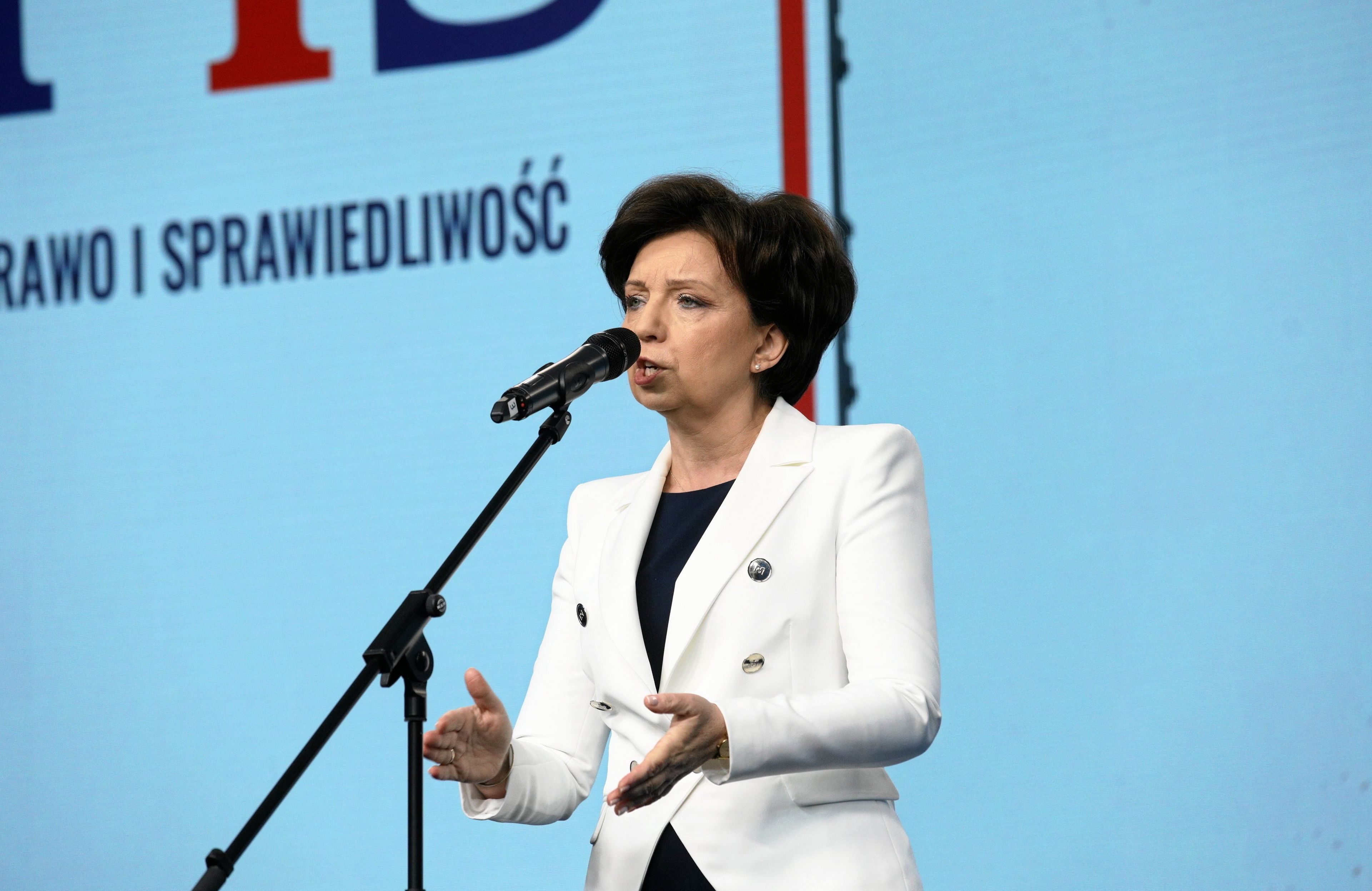 Marlena Maląg, stojący mikrofon, niebieskie tło i kawałek napisu Prawo i Sprawiedliwość