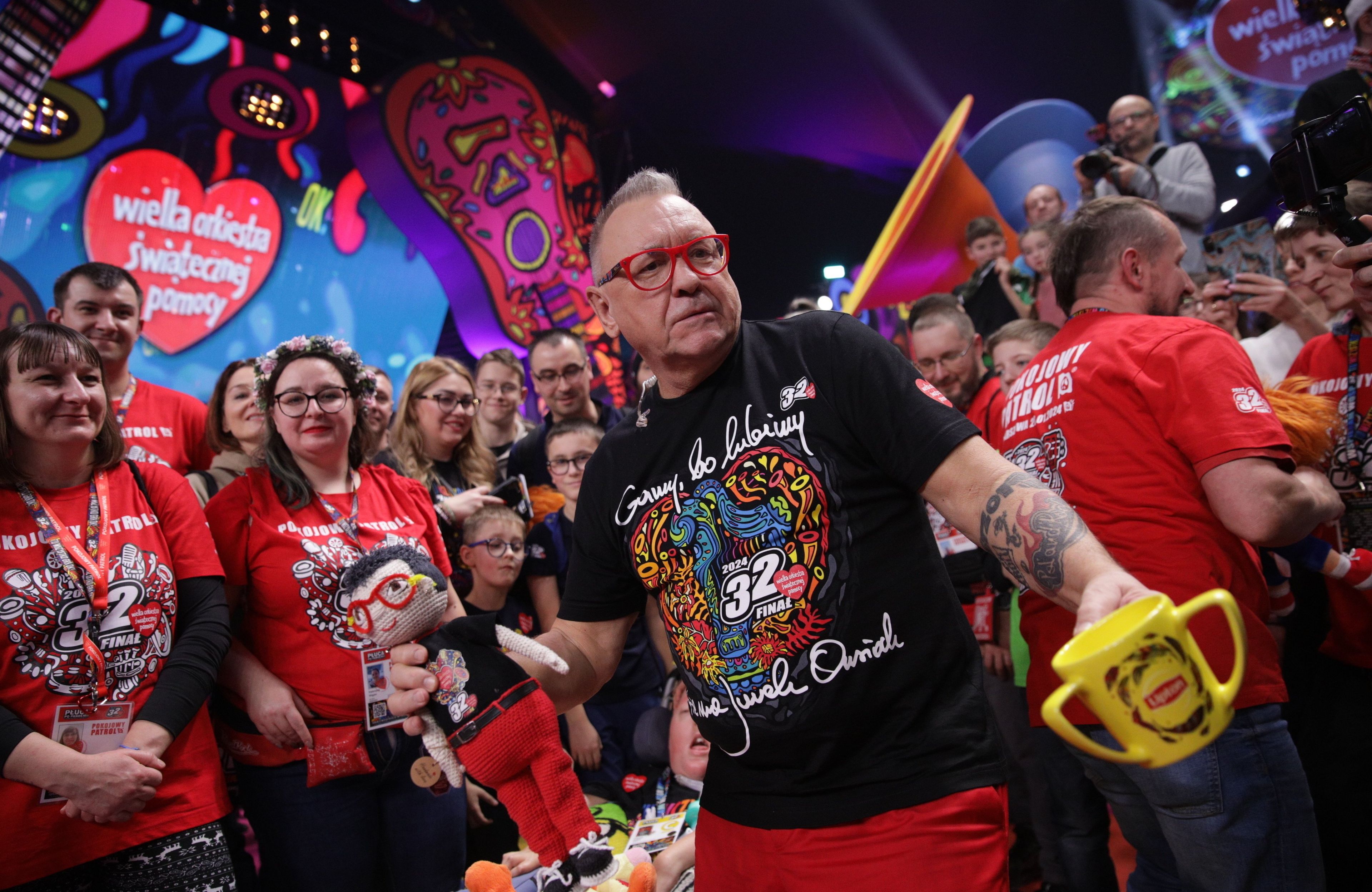 Jurek Owsiak w czerwonych okularach, za nim tłum osób i serduszko wośp