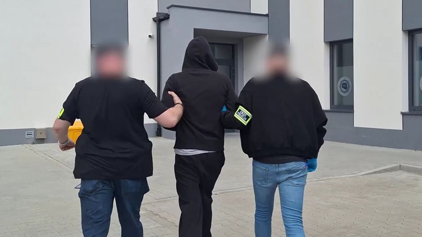 Trzy osoby widziane z tyłu . Dwóch policjantów w cywilu prowadzi zatrzymanego młodego mężczyznę.