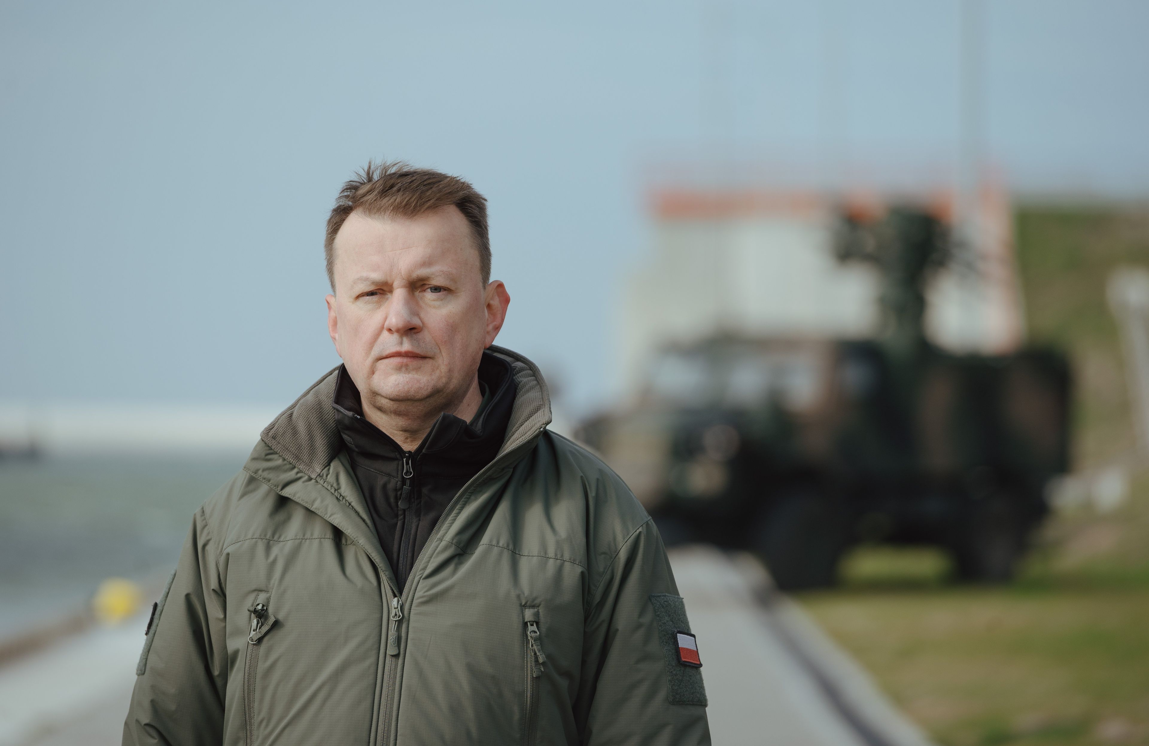 Mężczyzna na tle wojskowe sprzętu {Mariusz Błaszczak]