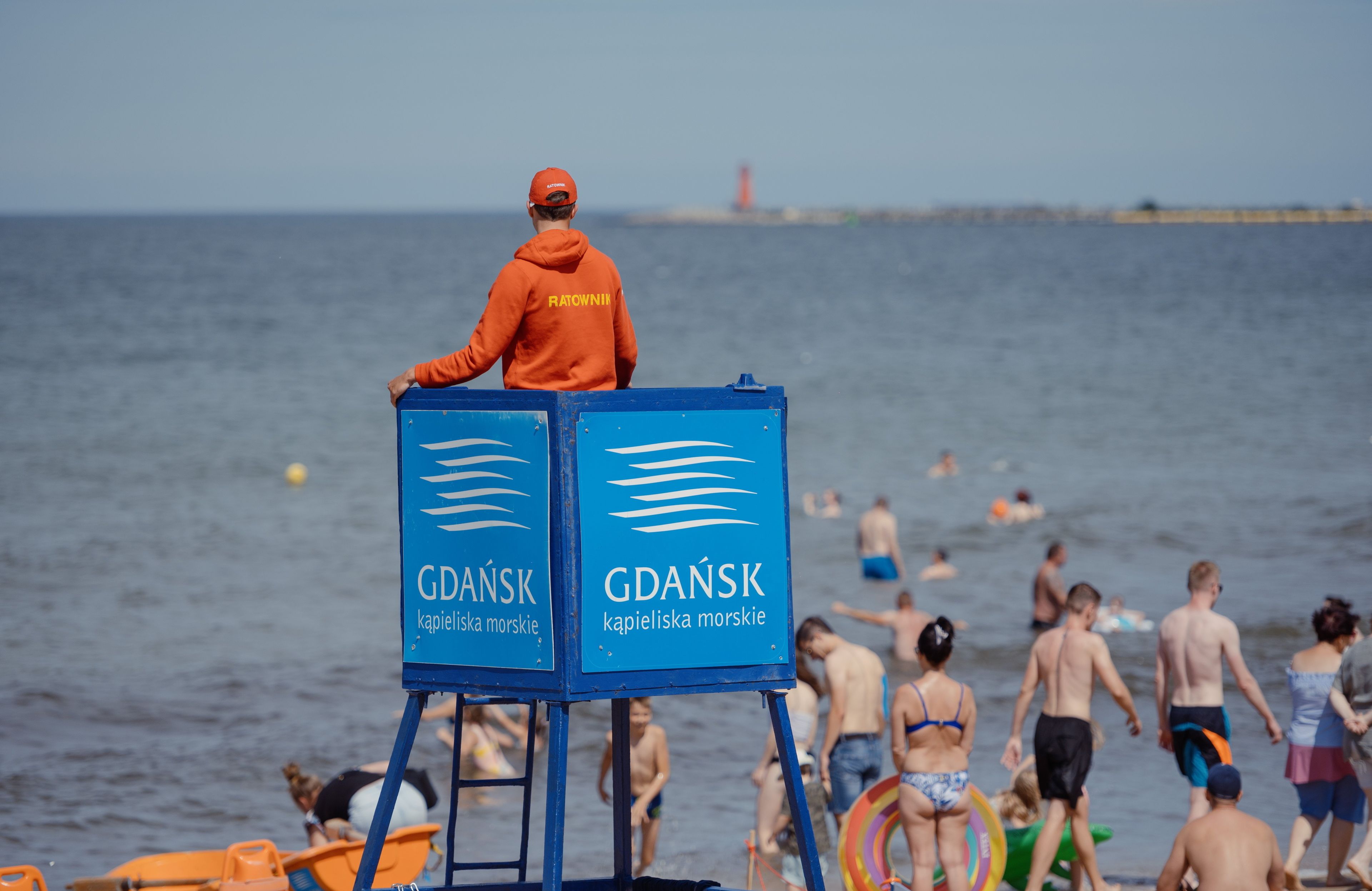 Ludzie na plaży, ratownik w pomarańczowej kurtce