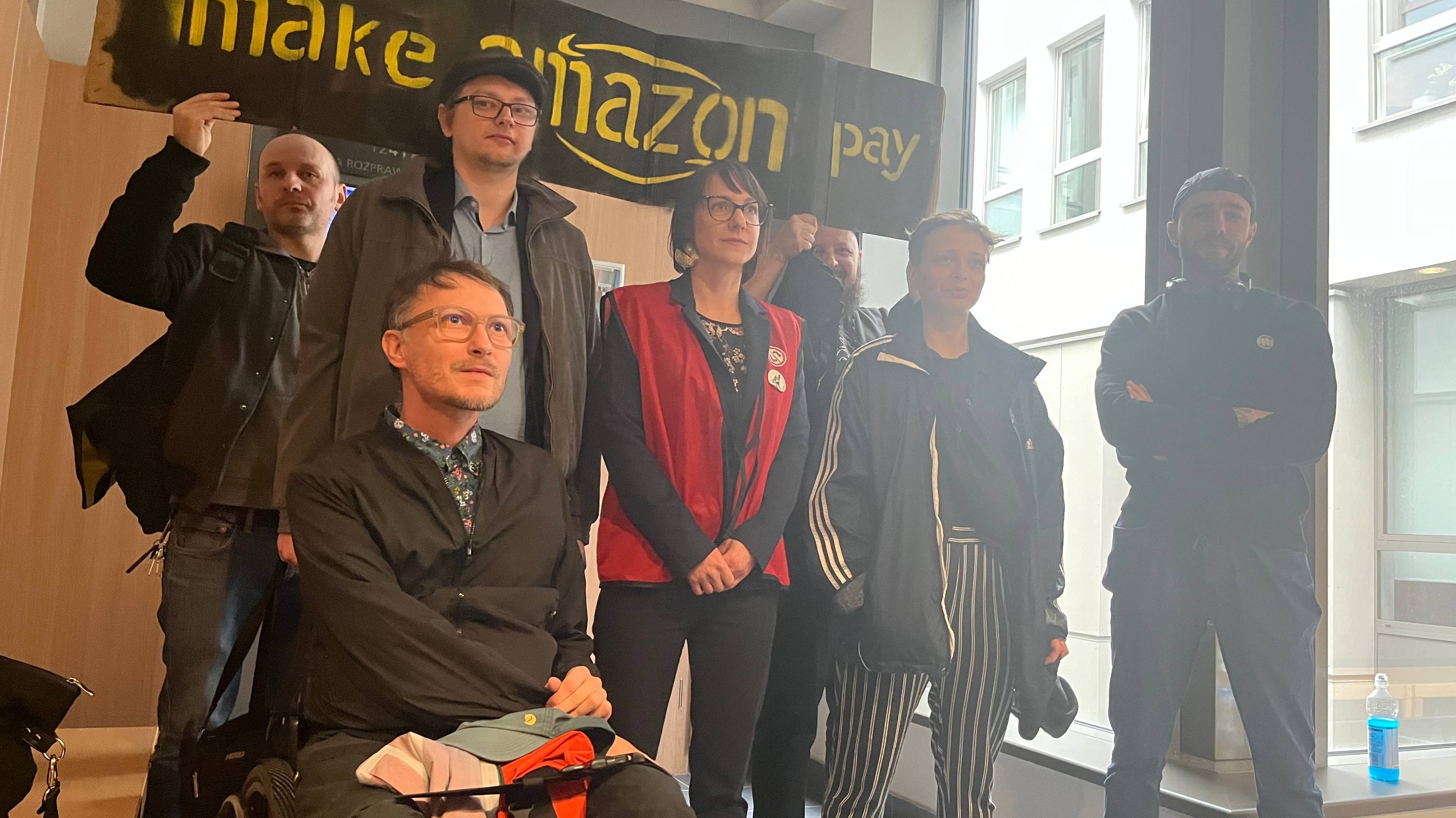 Ludzie stoją przed transparentem "Make amazon pay"