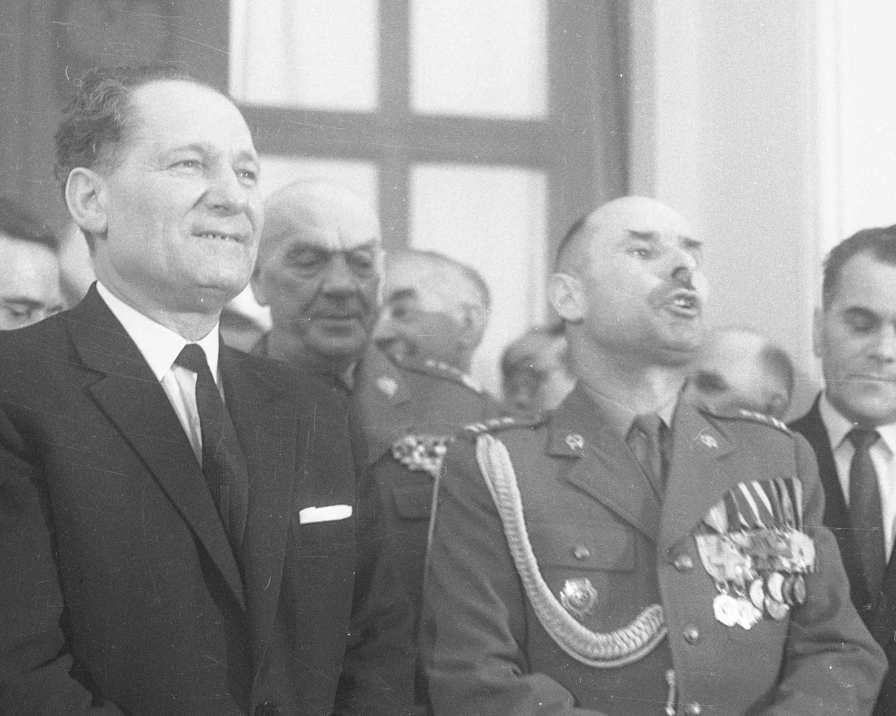 Mieczysław Moczar w garniturze stoi obok oficera w mundurze z medalami.
