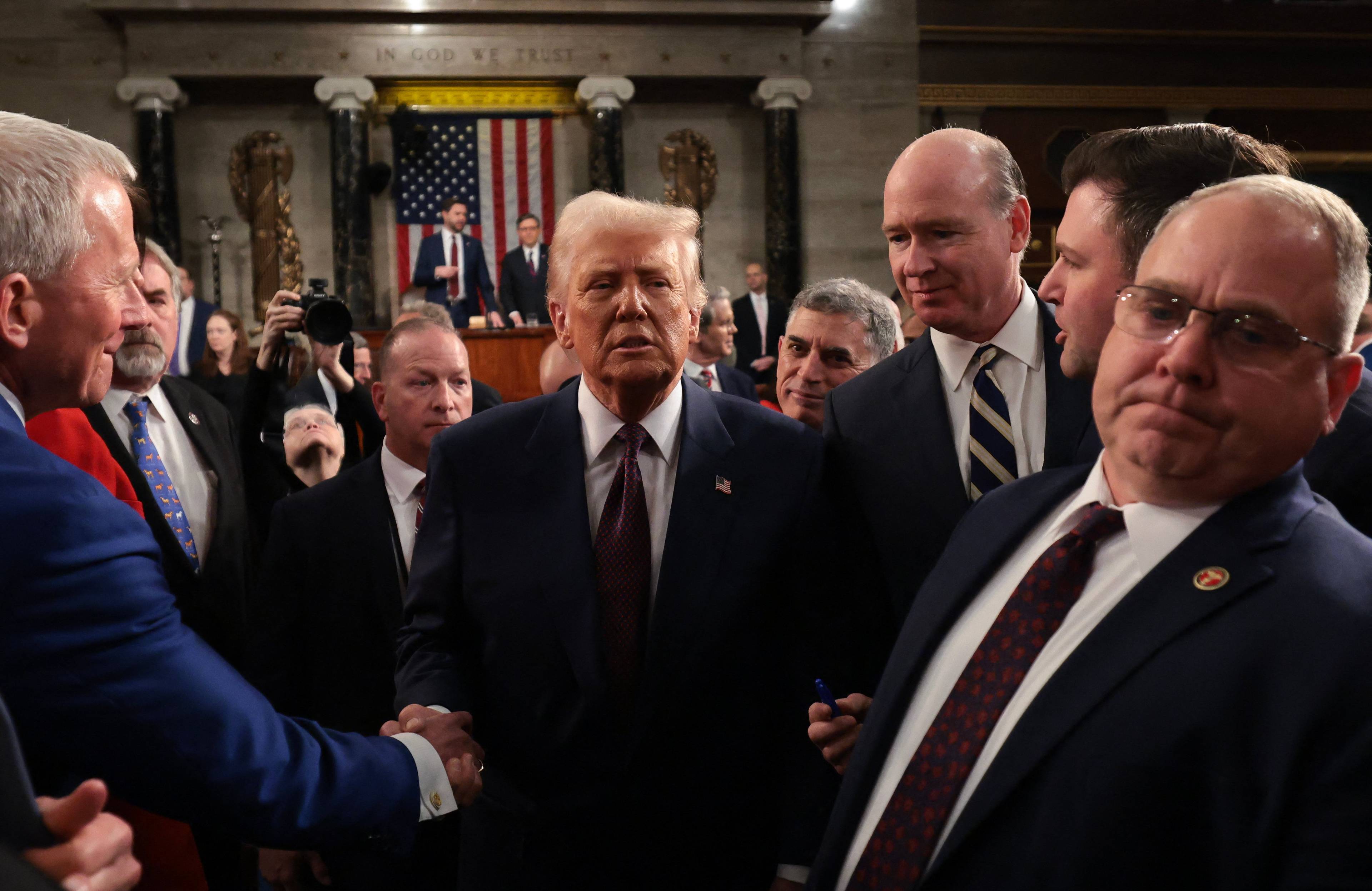 Donald Trump po przemówieniu w Kongresie ściska ręce słuchaczon. W tle mównica i flaga amerykańska