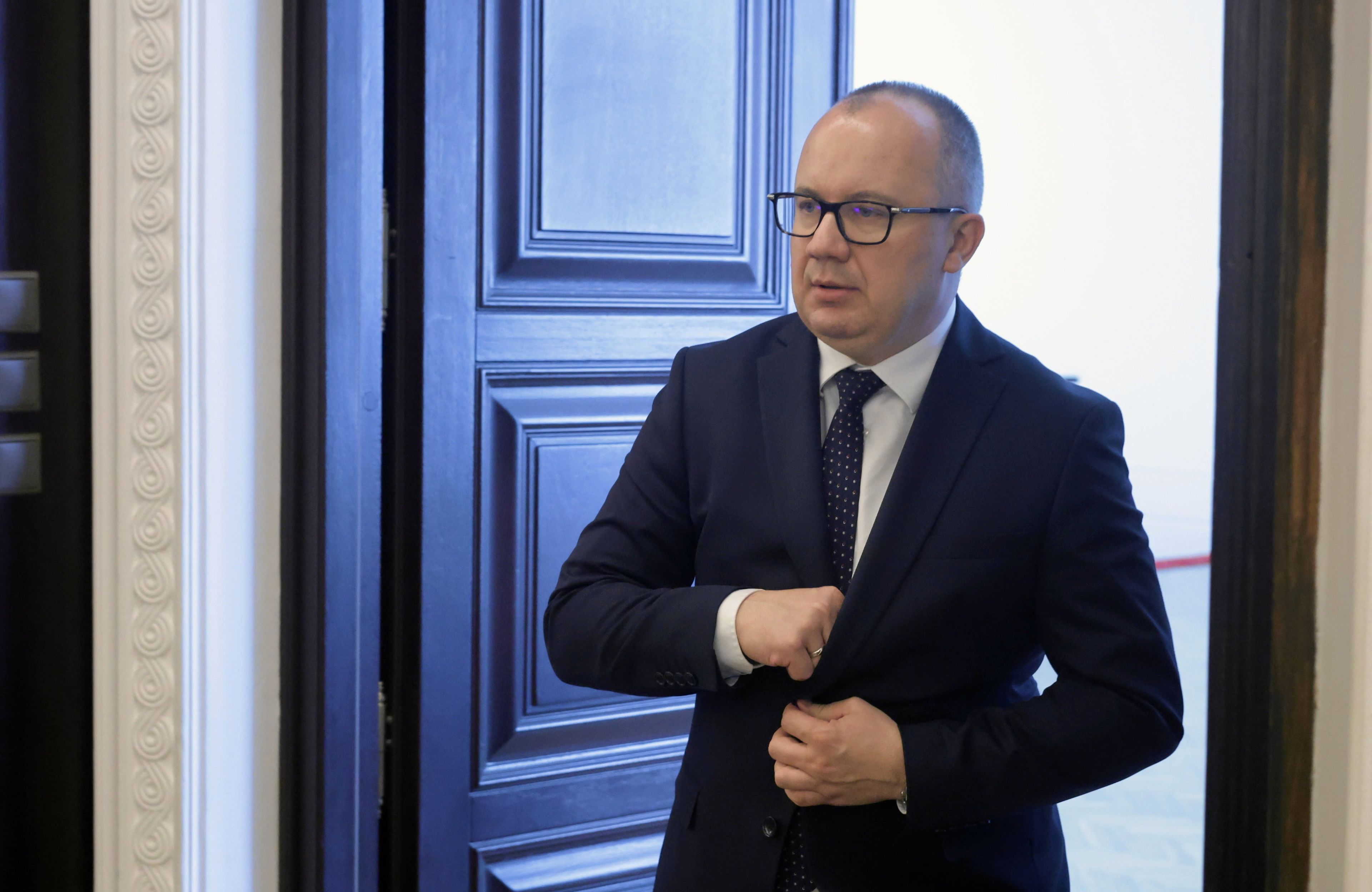 Mężczyzna w okularach wchodzi przez duże drzwi na salę posiedzeń rządu