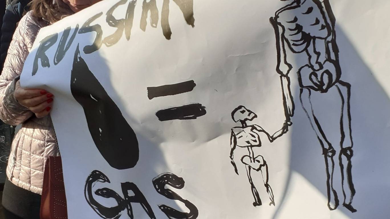 Demonstrant trzyma baner z napisem "Russian gas równa się sylwetka osoby dorosłej i dwójki dzieci, w domyśle uchodźcy