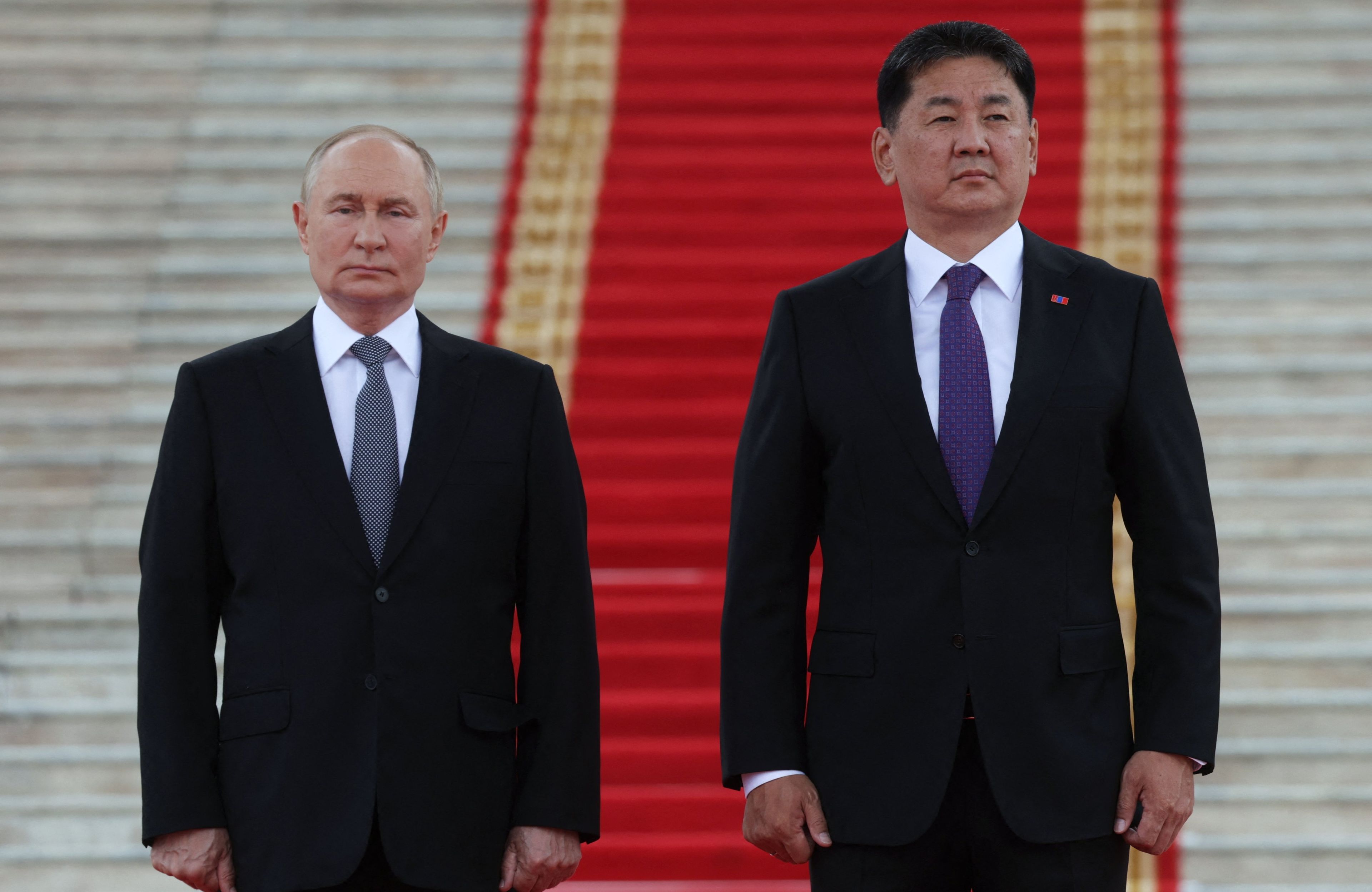 Prezydent Rosji Władimir Putin (po lewej) oraz prezydent Mongolii Uchnaagijn Chürelsüch w czarnych garniturach stoją na tle wysokich schodów przykrytych czerwonym dywanem i pozują do oficjalnych zdjęć z wizyty państwowej Putina w Mongolii