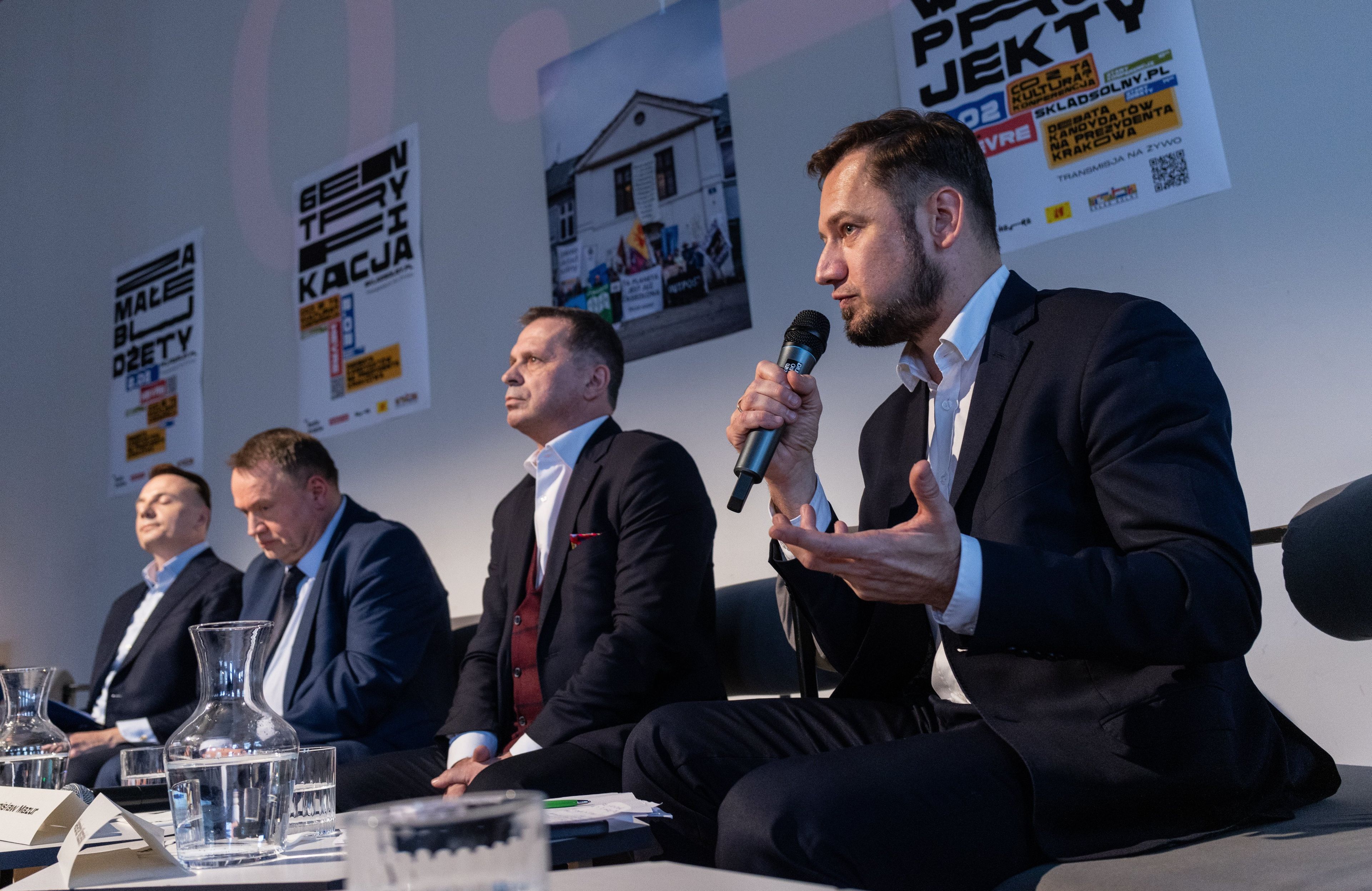Kandydaci na prezydenta Krakowa za stołem podczas debaty. Na pierwszym planie Aleksander Miszalski, pierwszy od lewej Łukasz Gibała