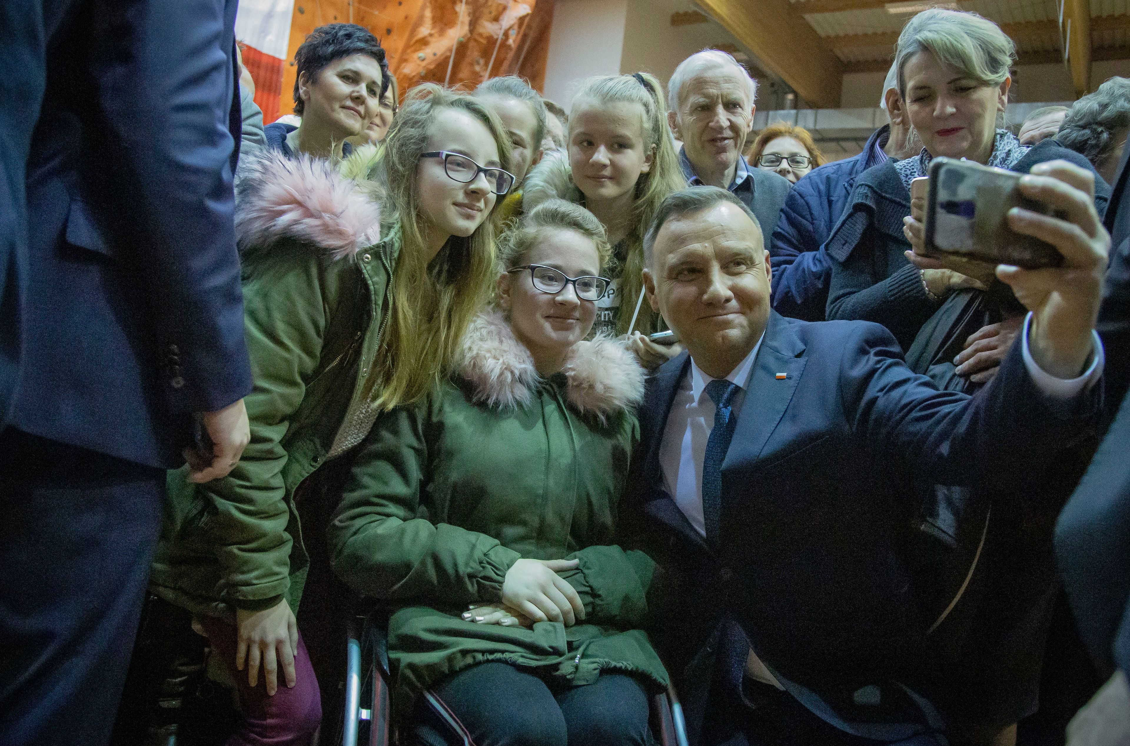 Uśmiechnięty mężczyzna w średnim wieku robi sobie selfie z dziewczyną na wózku. To Andrzej Duda