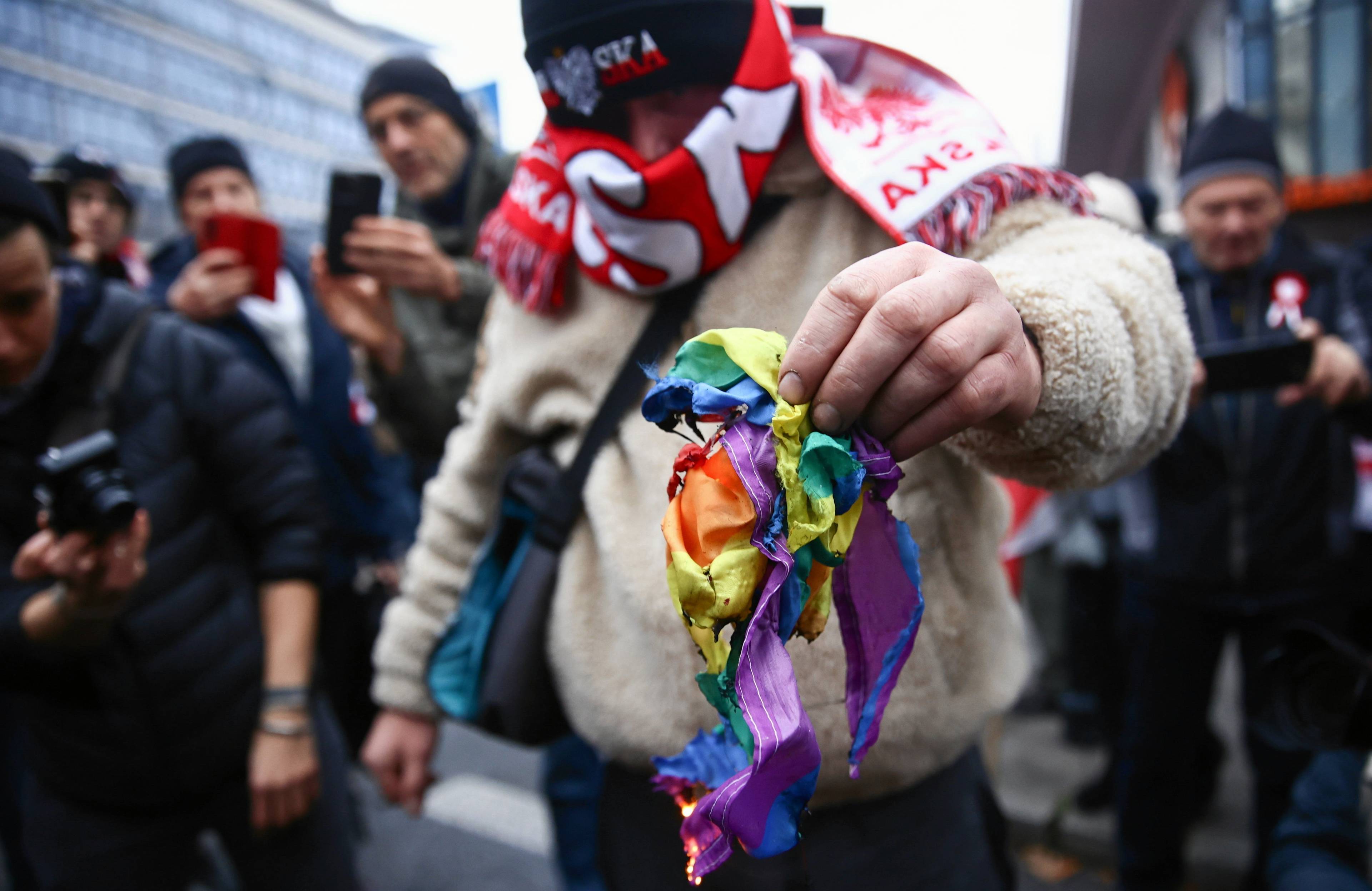 Uczestnik Marszu Niepodległości w Warszawie pali tęczową flagę, symbol społeczności LGBT+