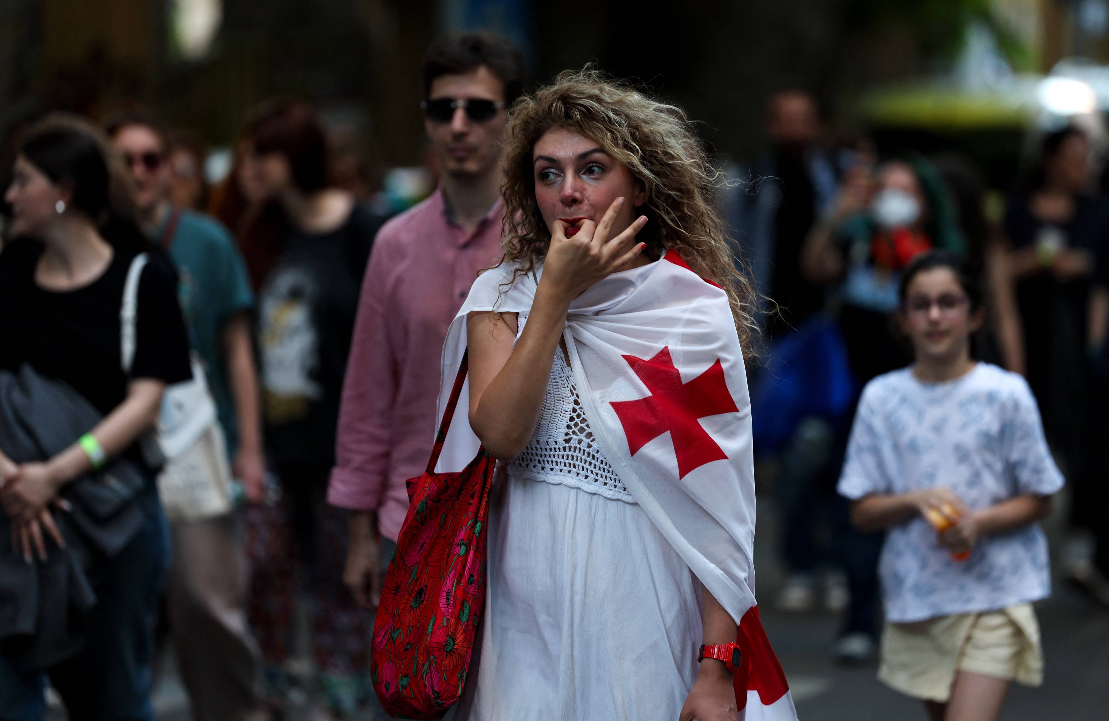 Kobieta owinięta w gruzińską flagę gwiżdże na palcach