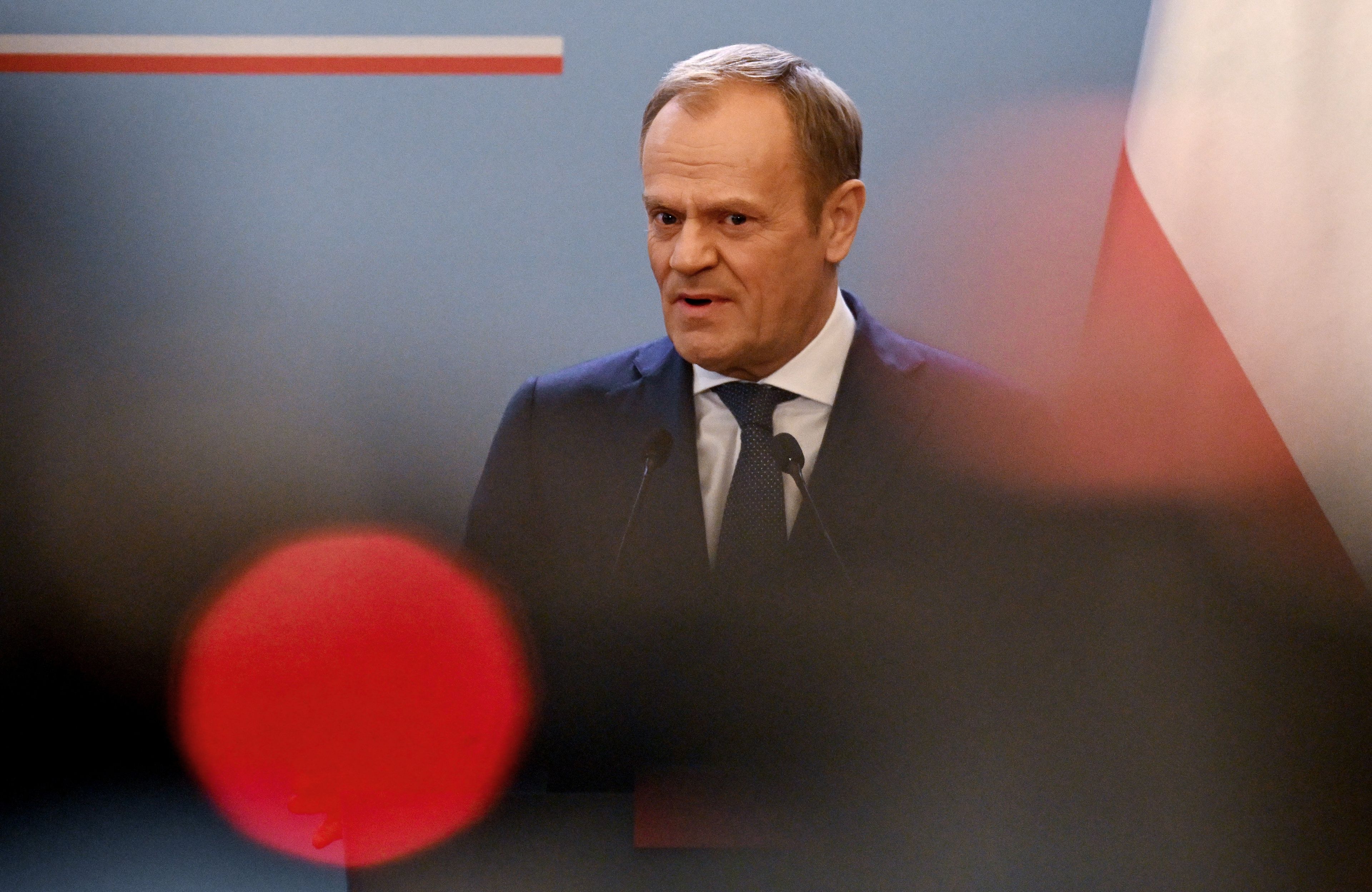 Donald Tusk na tle biało-czerwonej flagi