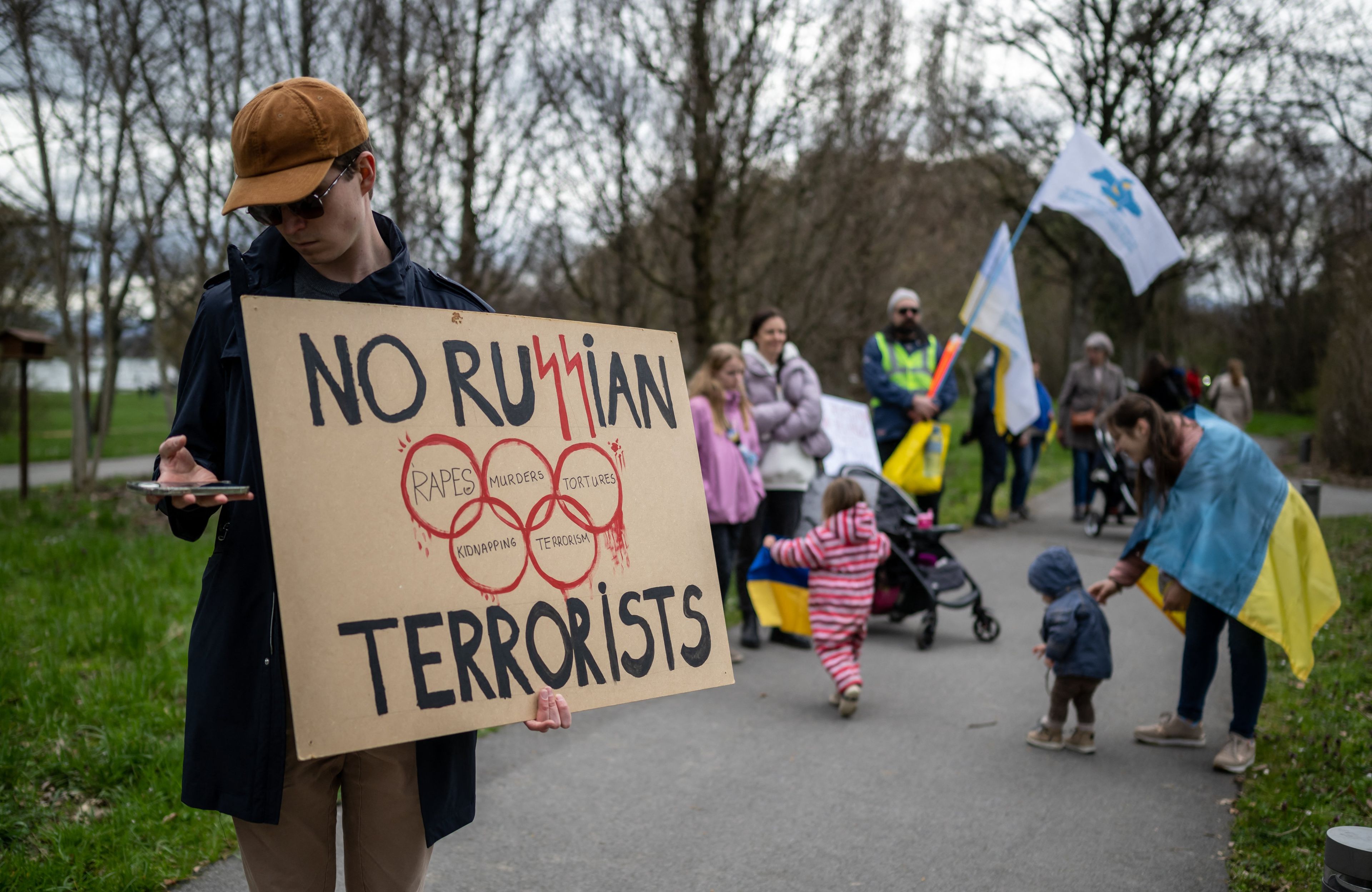 Demonstranci trzymają transparent: No ru$$ian terrorist" ze znakiem kół olimpijskich